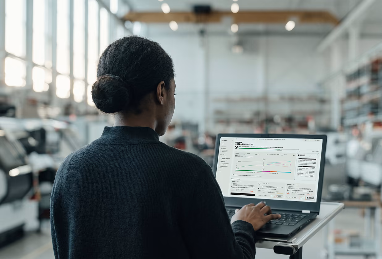 Person with hair in a bun using a laptop showing a dashboard with graphs and data in an industrial or workshop setting.