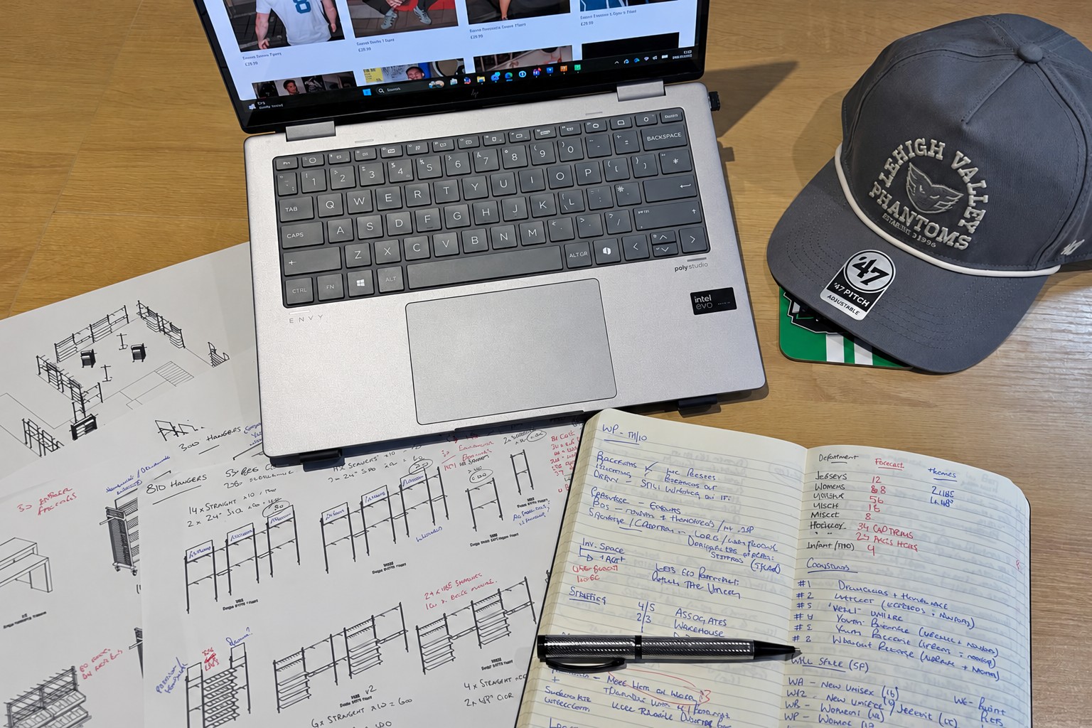 Sports merchandise planning workspace with a laptop, retail layouts and notebook.
