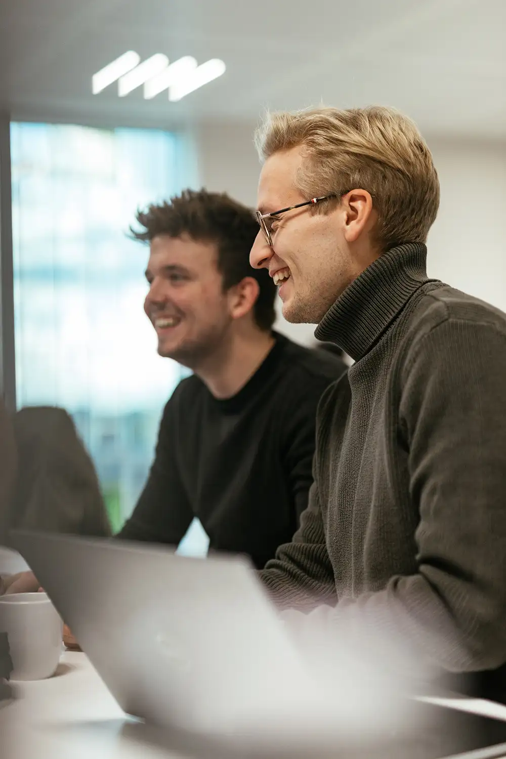 Two men sit at a table during a meeting, smiling and engaged in conversation.