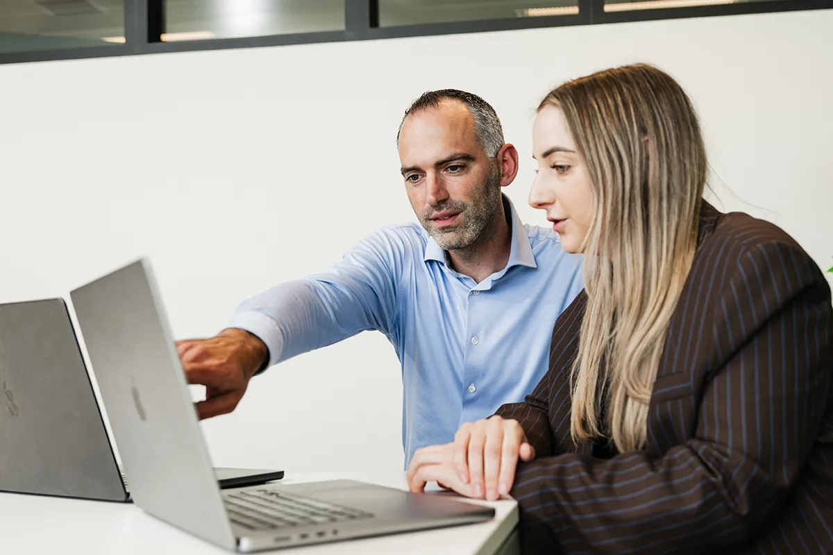 Two colleagues collaborate at a laptop in a modern office.