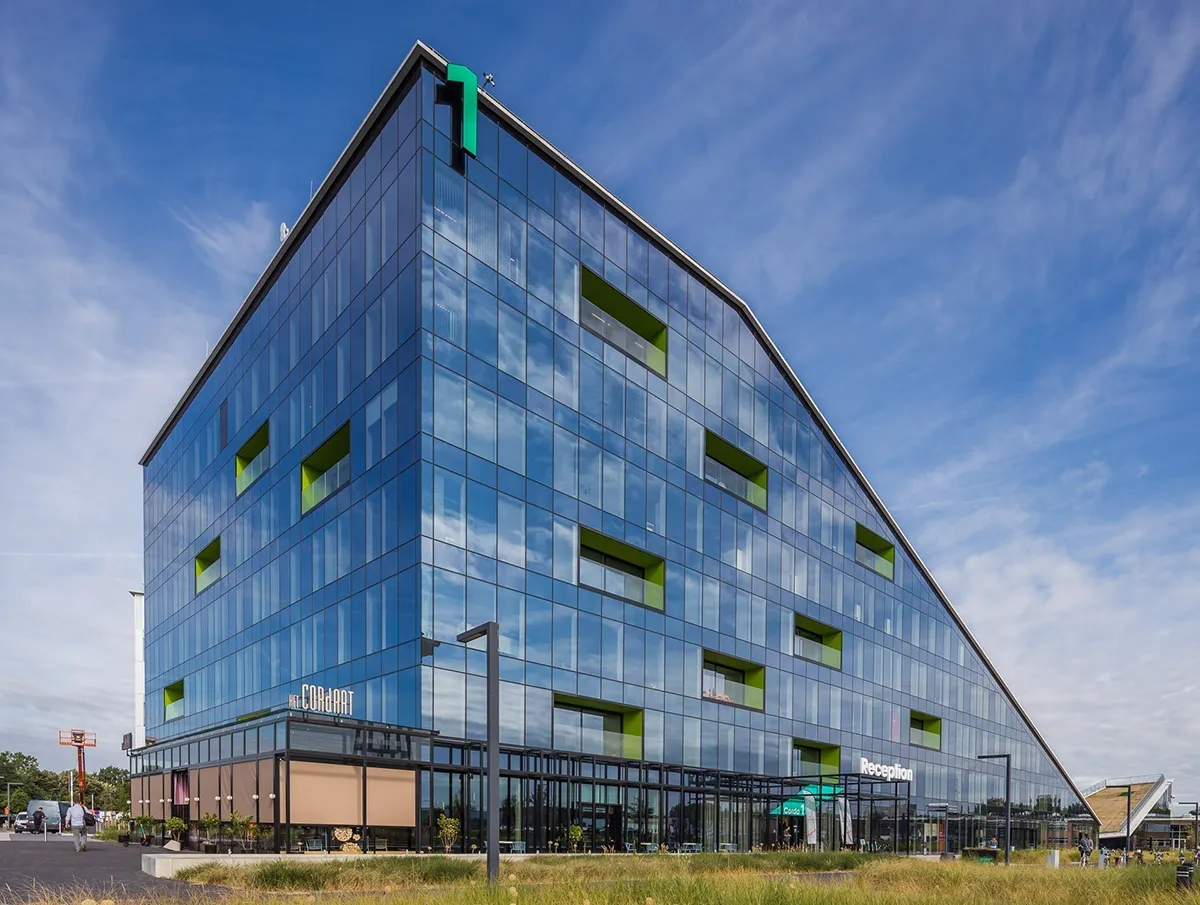Contemporary angular office building with blue glass windows and green accents under a clear sky.