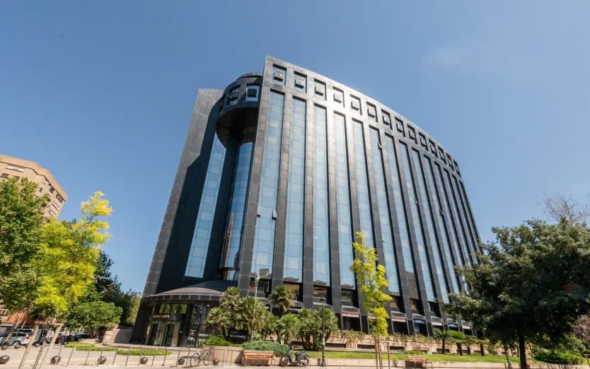 Tall curved office building with reflective glass windows, framed by trees under a clear blue sky.