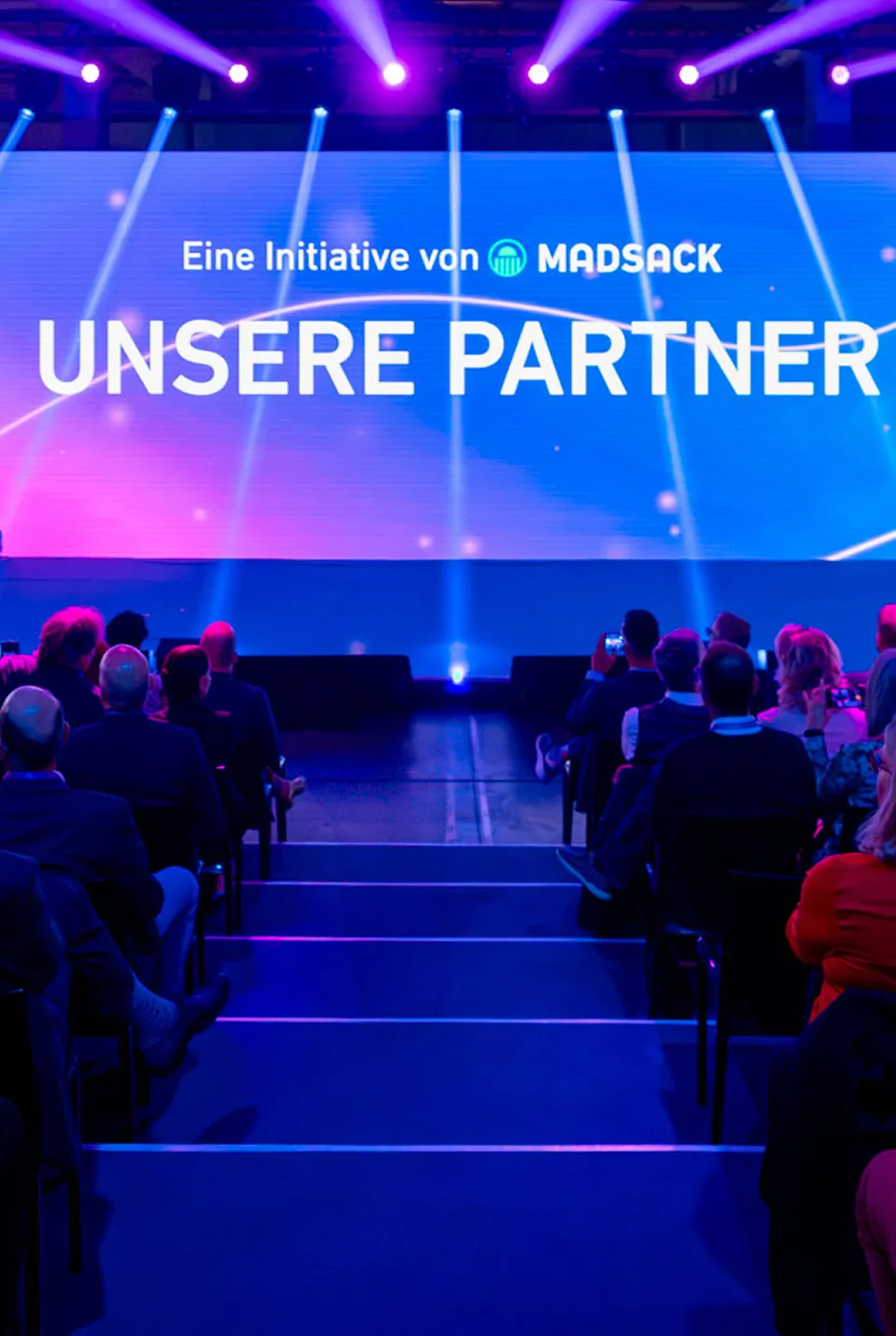 Publikum vor der Bühne mit der Leinwand „Unsere Partner“