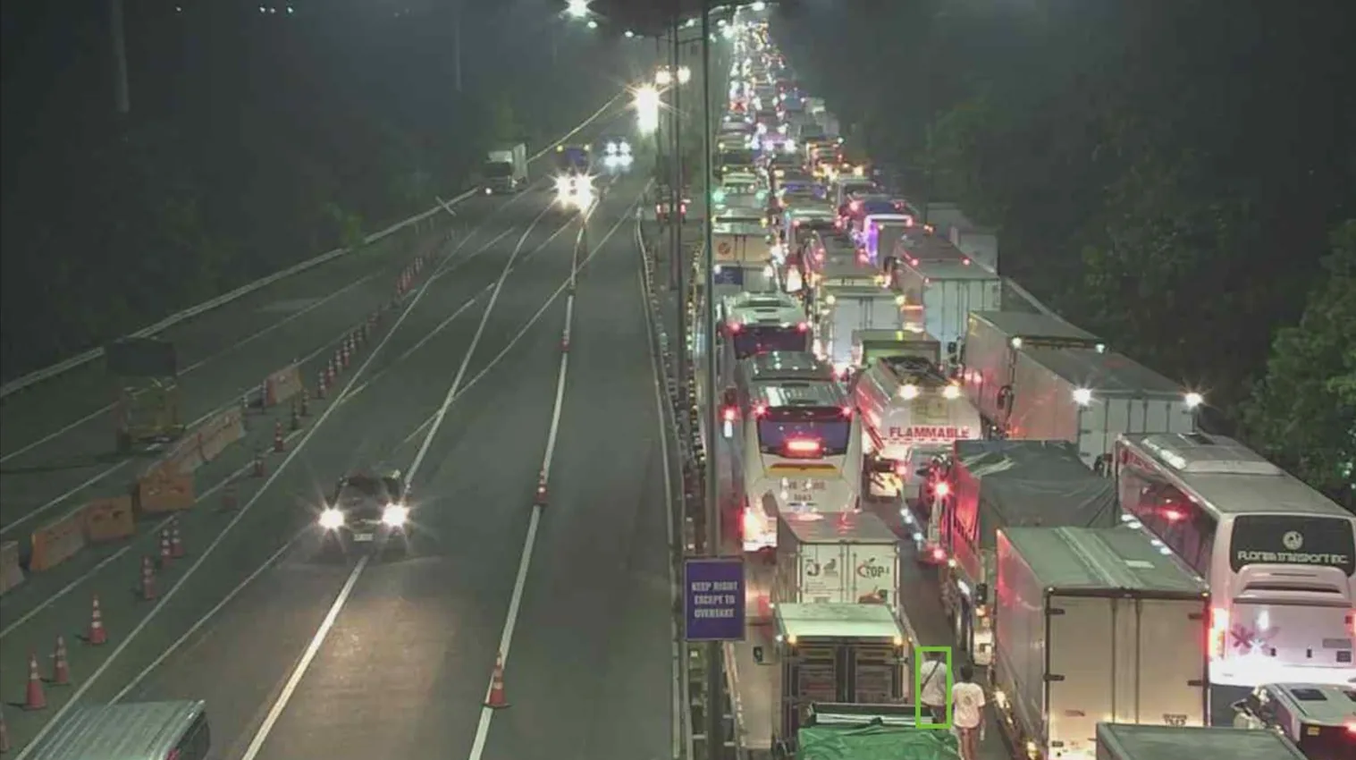 Imagen de cámara de autopista nocturna con una fila de camiones y autobuses detenidos y una persona en la calzada marcada por un cuadro de detección
