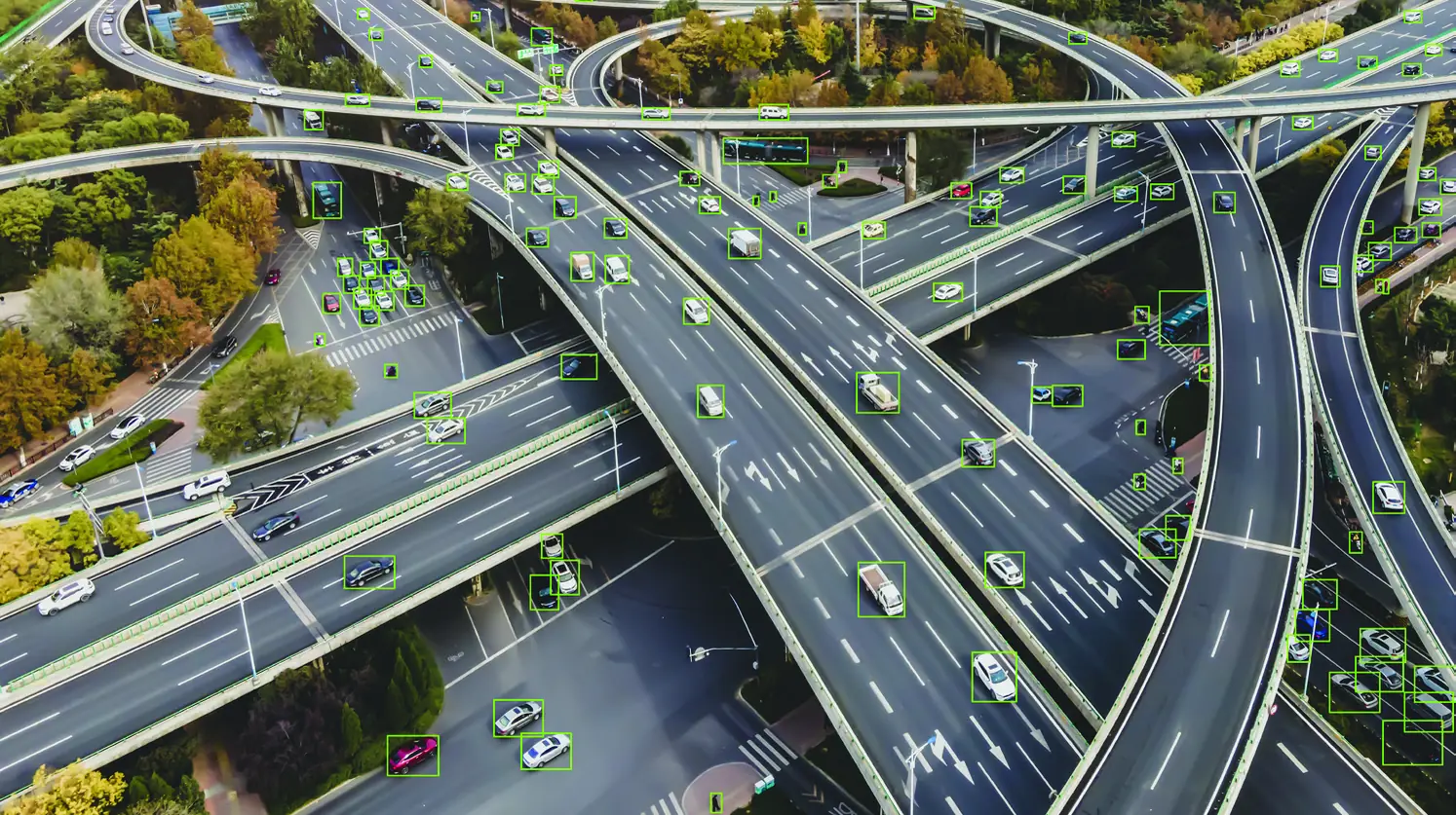 Aerial view of a multi-level highway interchange with each detected vehicle outlined by a green bounding box