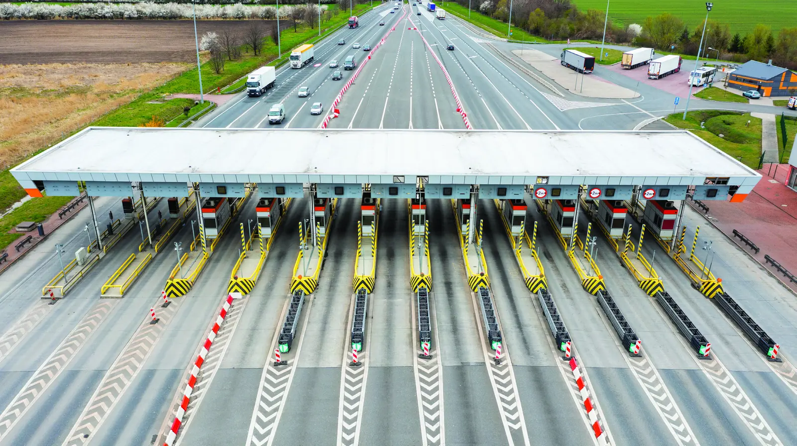 Aerial view of a highway toll plaza with a canopy over its lanes and vehicles lined up at the booths