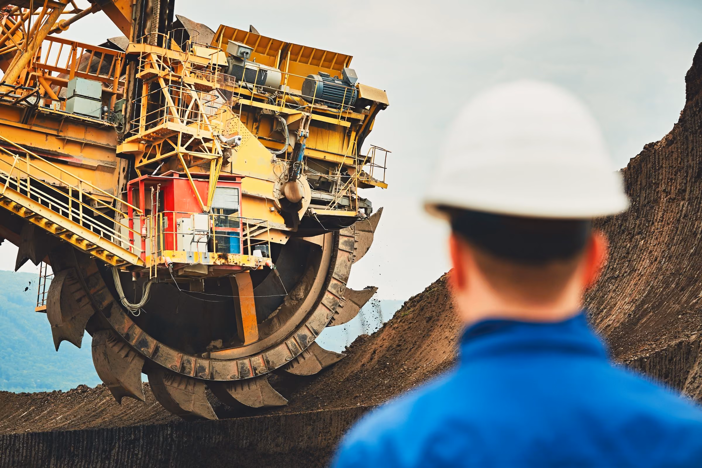 A worker in a hard hat looking up at a bucket-wheel excavator in an open pit