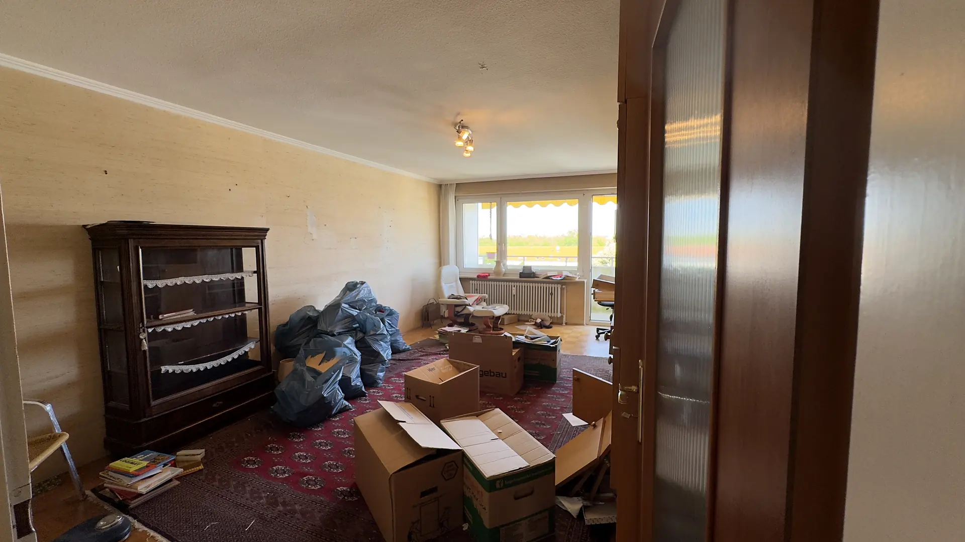 Wohnzimmer bei einer Wohnungsauflösung: Vitrine, Umzugskartons und gepackte Säcke