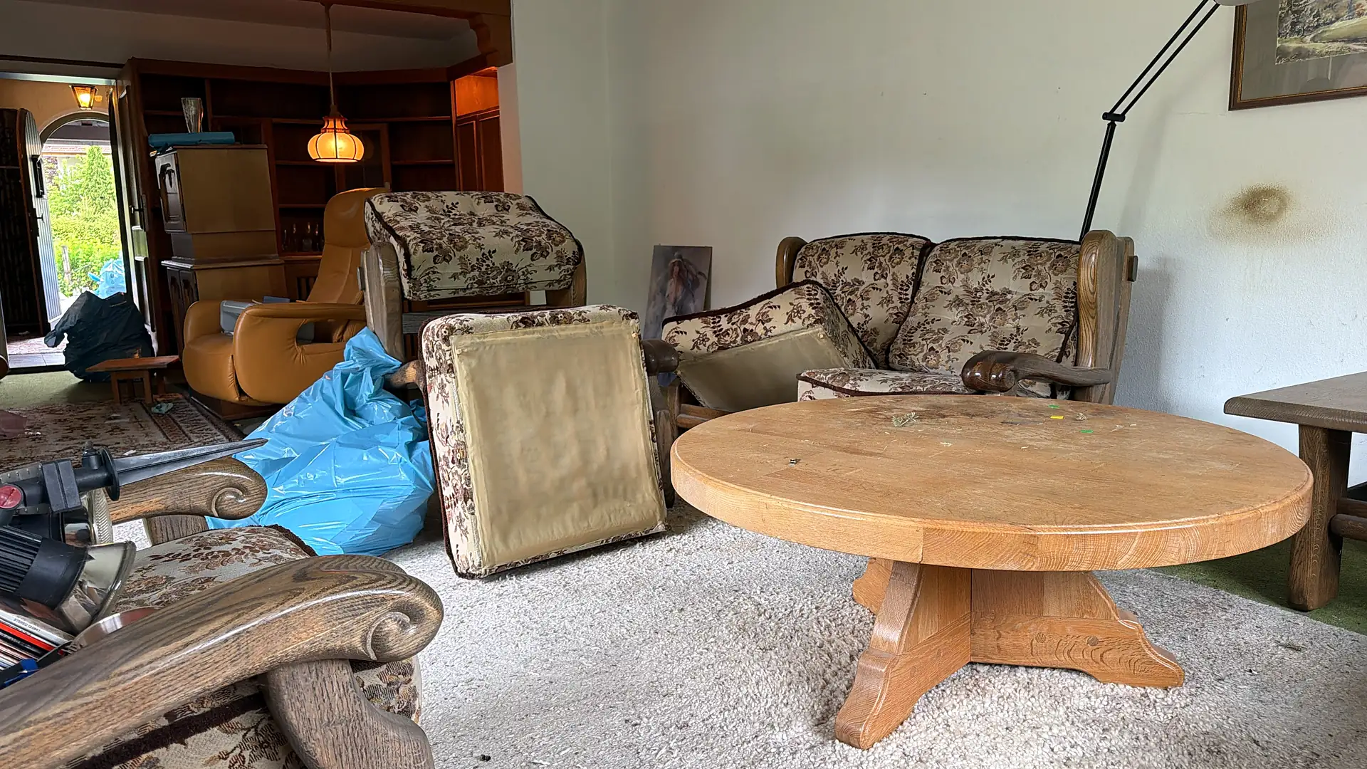Wohnzimmer während einer Haushaltsauflösung: Sessel, runder Couchtisch und Säcke