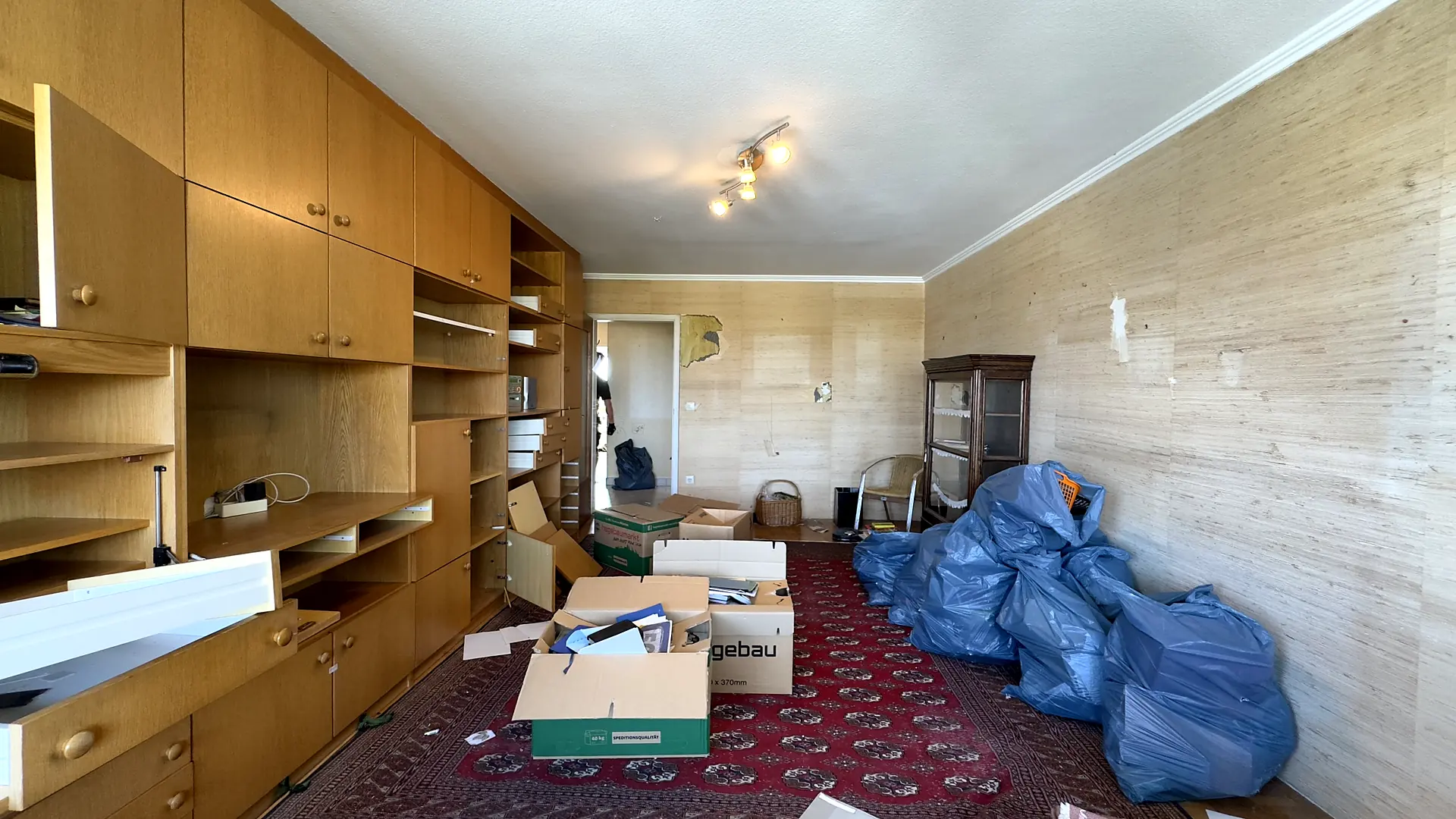 Wohnzimmer bei einer Wohnungsauflösung: leere Schrankwand, Kartons und gepackte Säcke