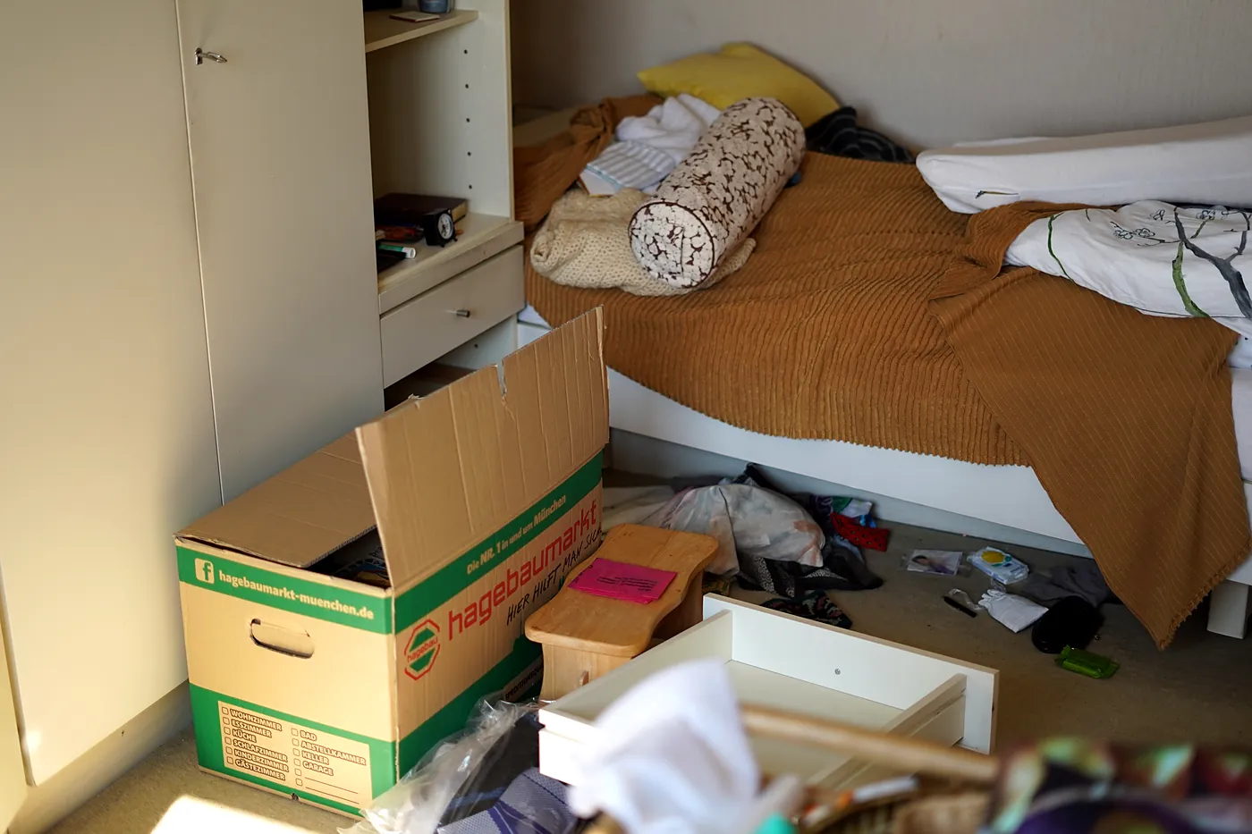 Schlafzimmer mit Umzugskarton und ausgeräumten Schubladen bei einer Wohnungsauflösung
