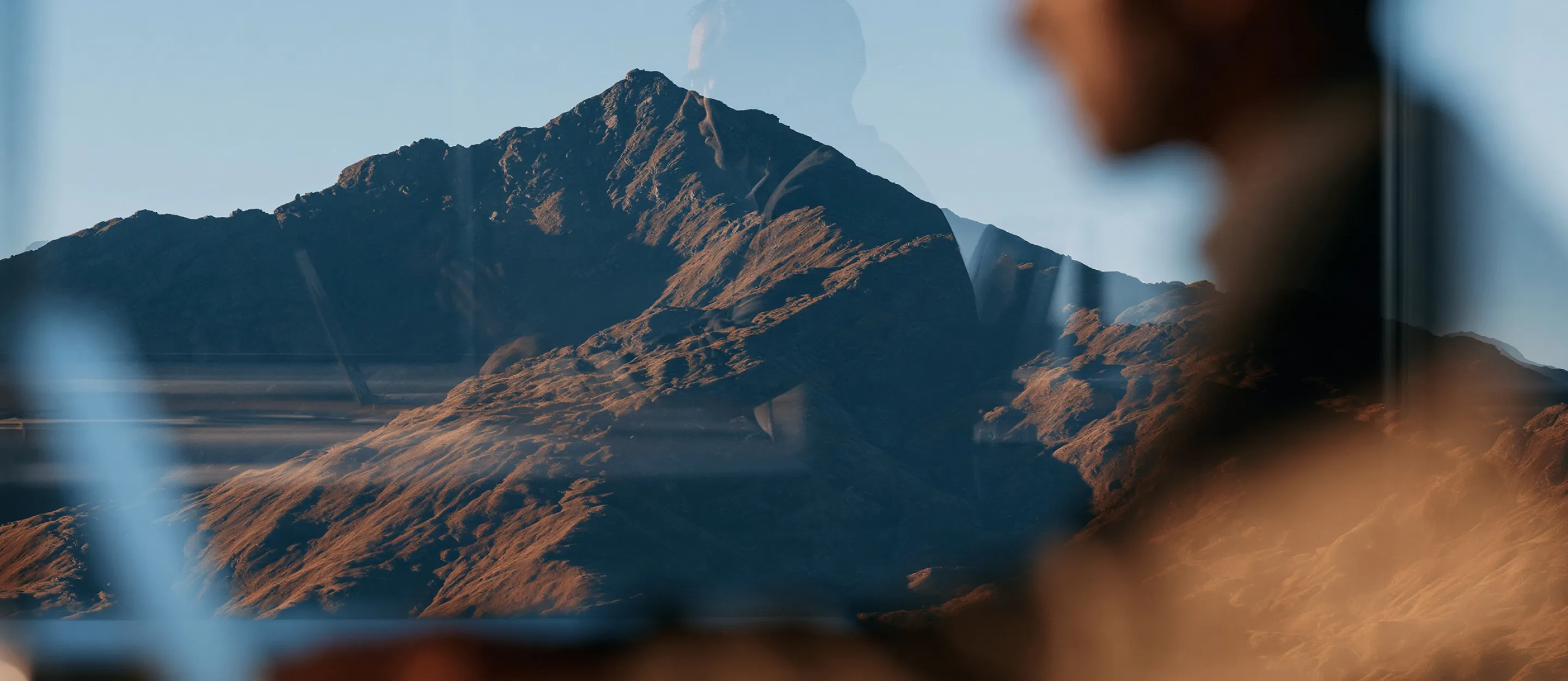 A sunlit mountain peak with a person at work reflected in glass