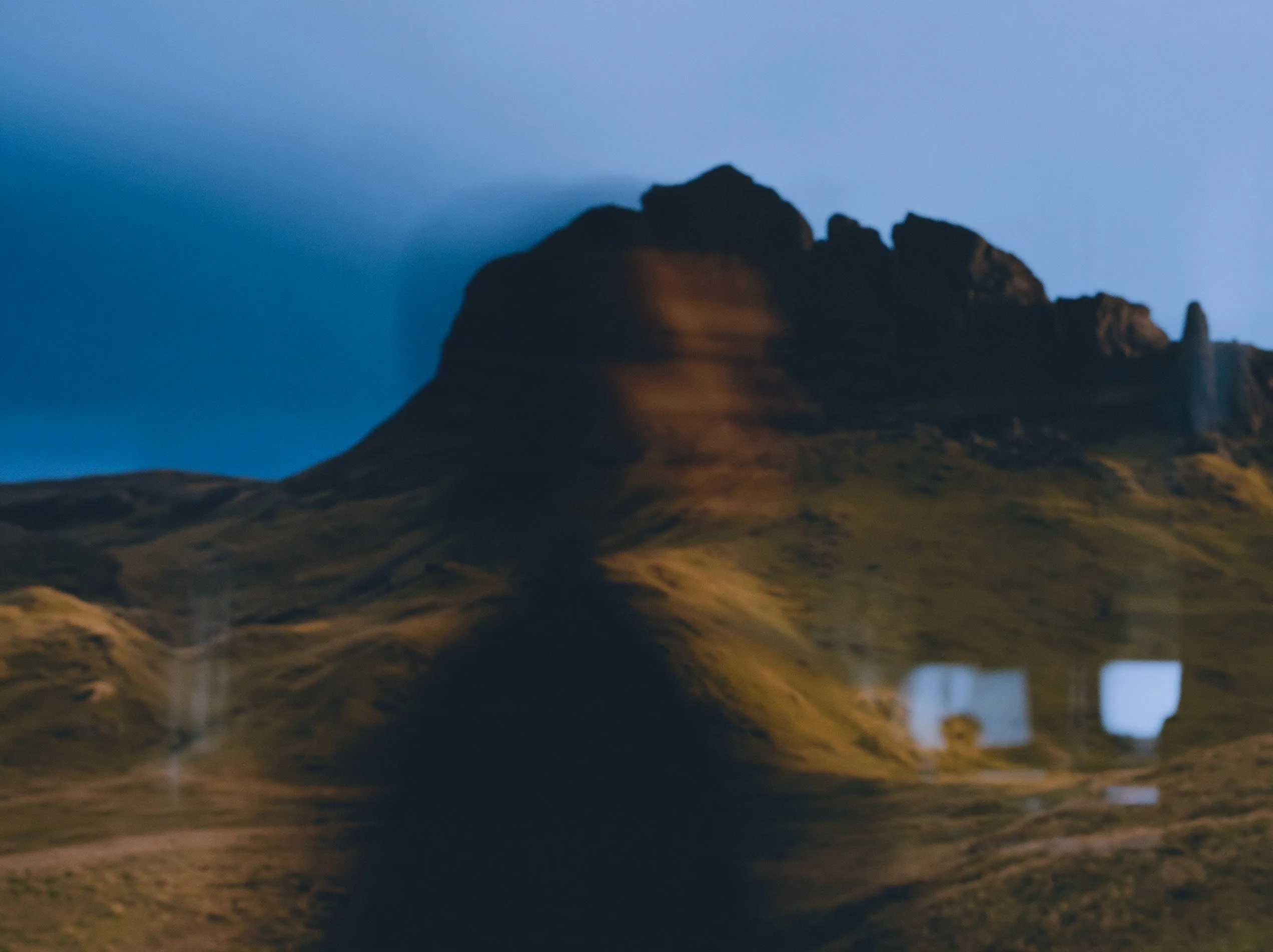 Rock pillars above a sunlit grassy slope, with a person reflected in window glass