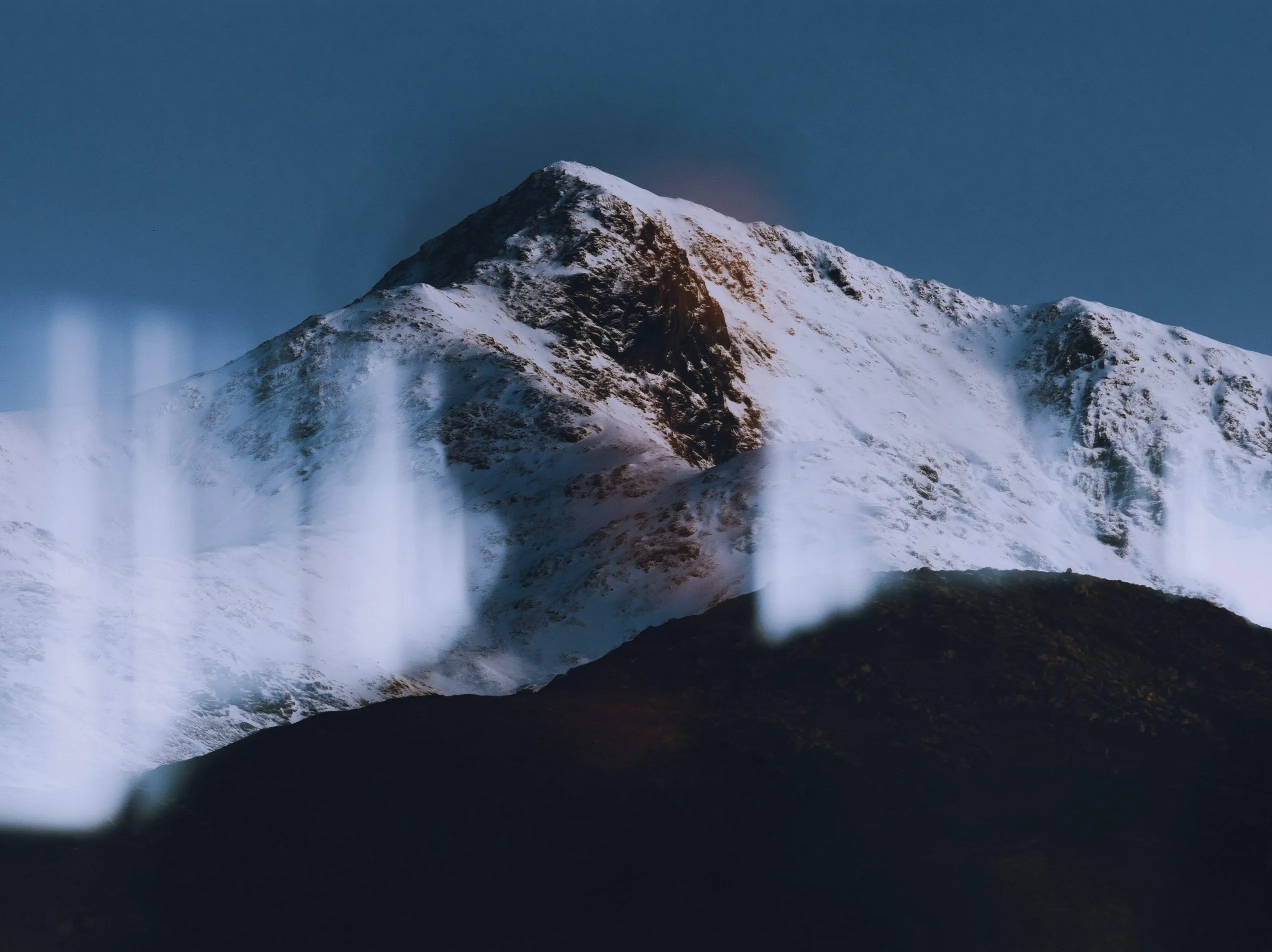 Snow-covered summit under a deep blue sky, with office lights reflected in window glass