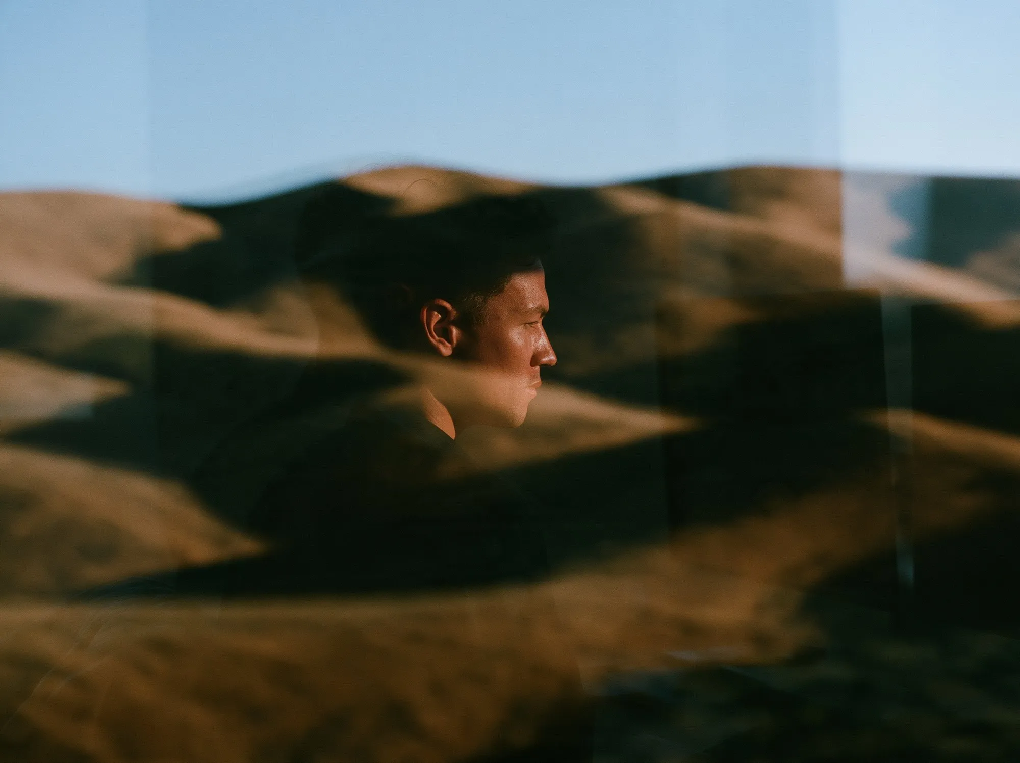 A colleague reflected in office glass over sunlit dry hills