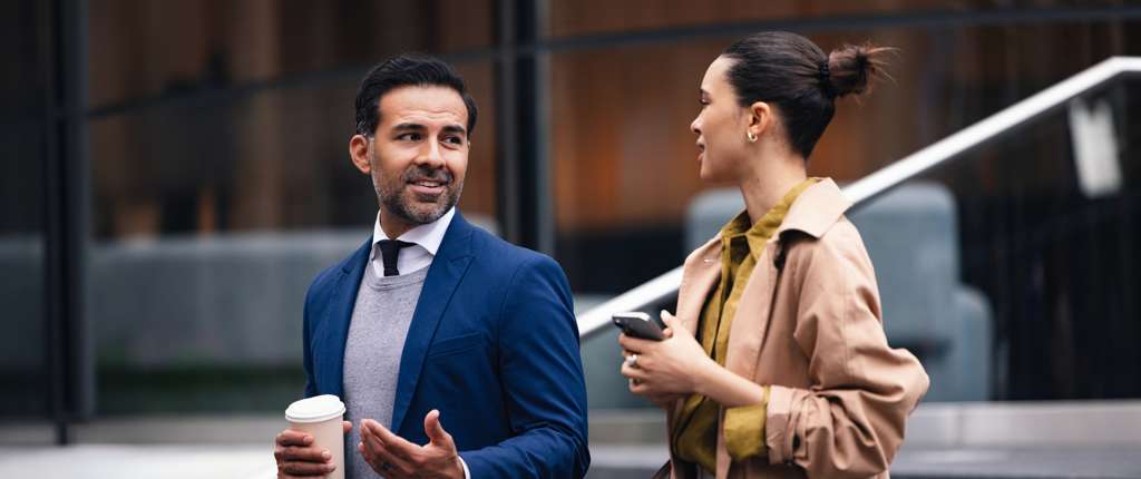 Two colleagues talk while walking outside an office building.