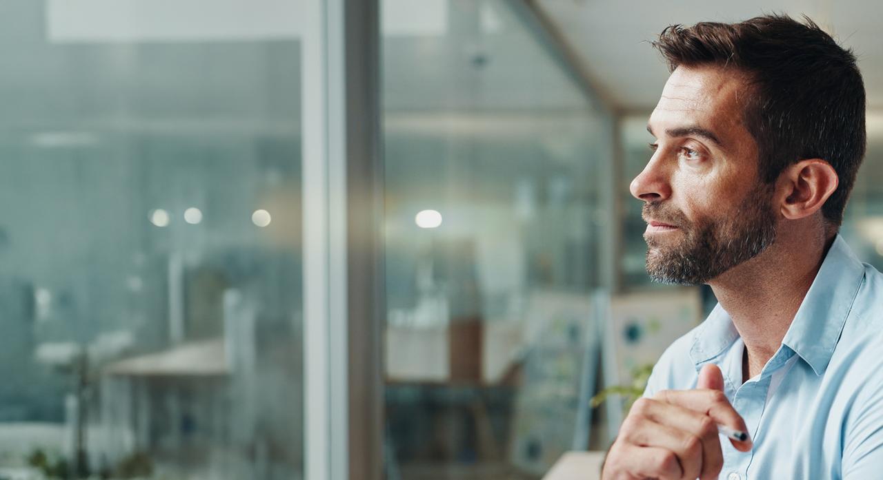 A man looks thoughtfully across an office.