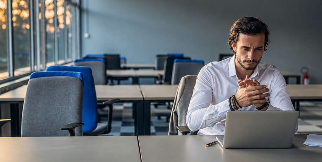 A man considers his work beside a laptop in an office.