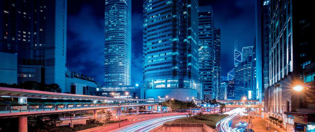 Traffic light trails run through a city financial district at night.