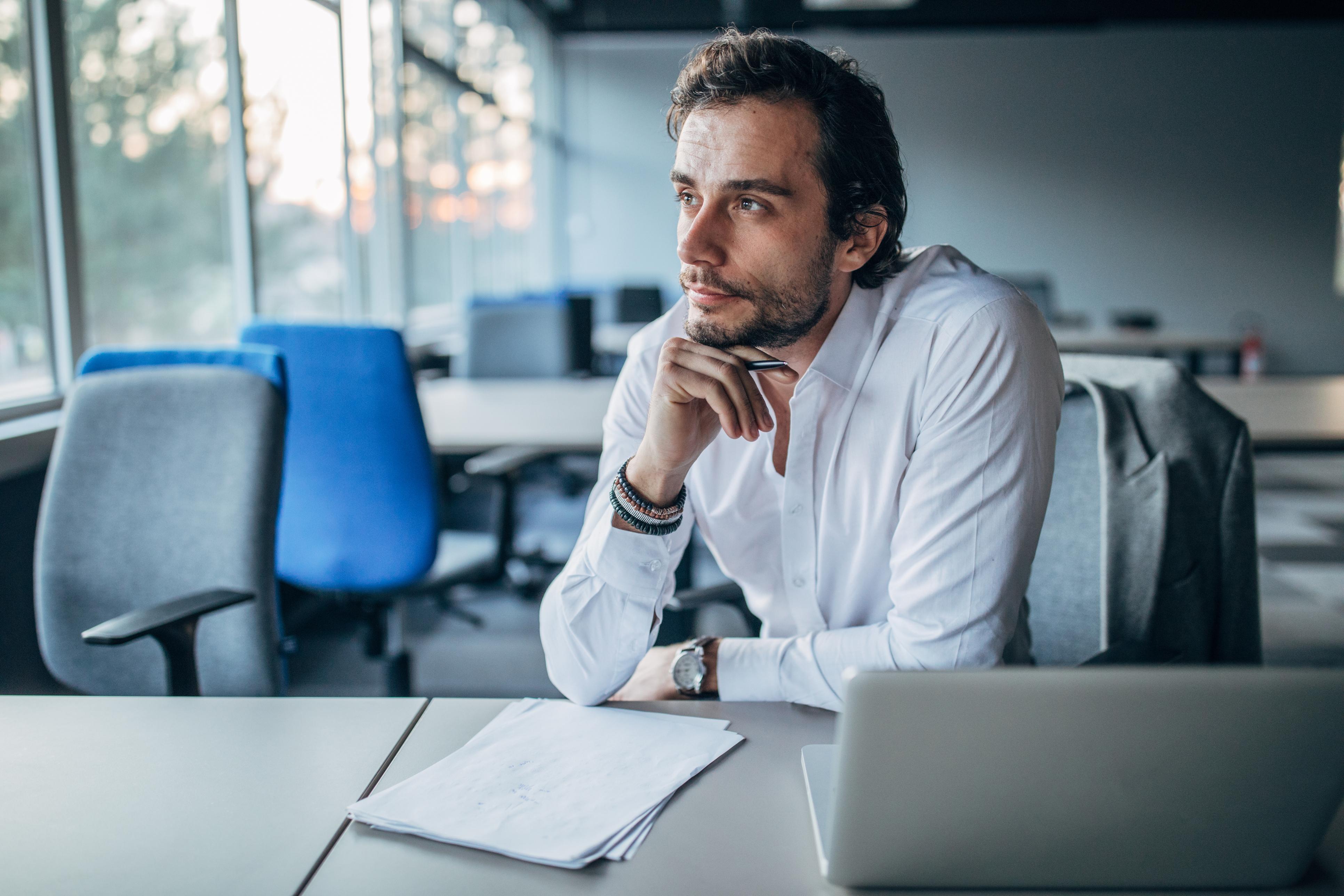 A man considers his work beside a laptop in an office.