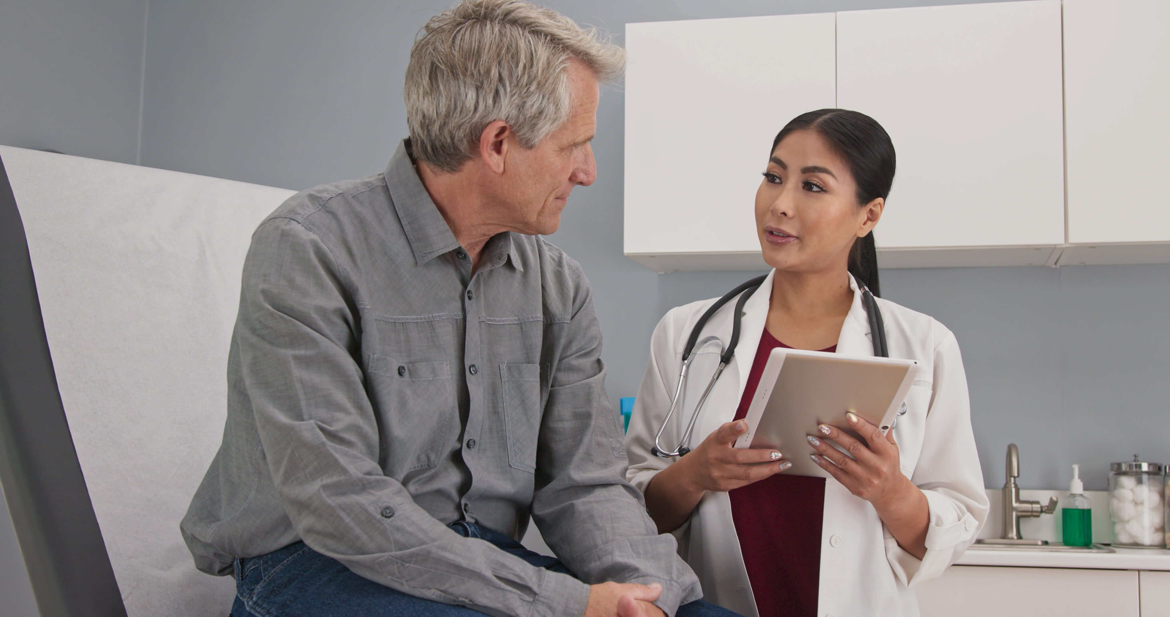 Older man meeting with a physician who is holding a tablet