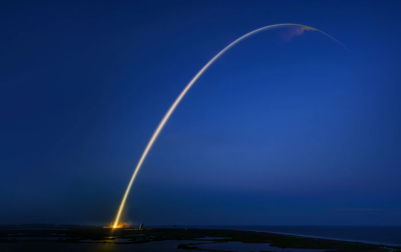 Rocket launch trail arcing across a deep blue evening sky