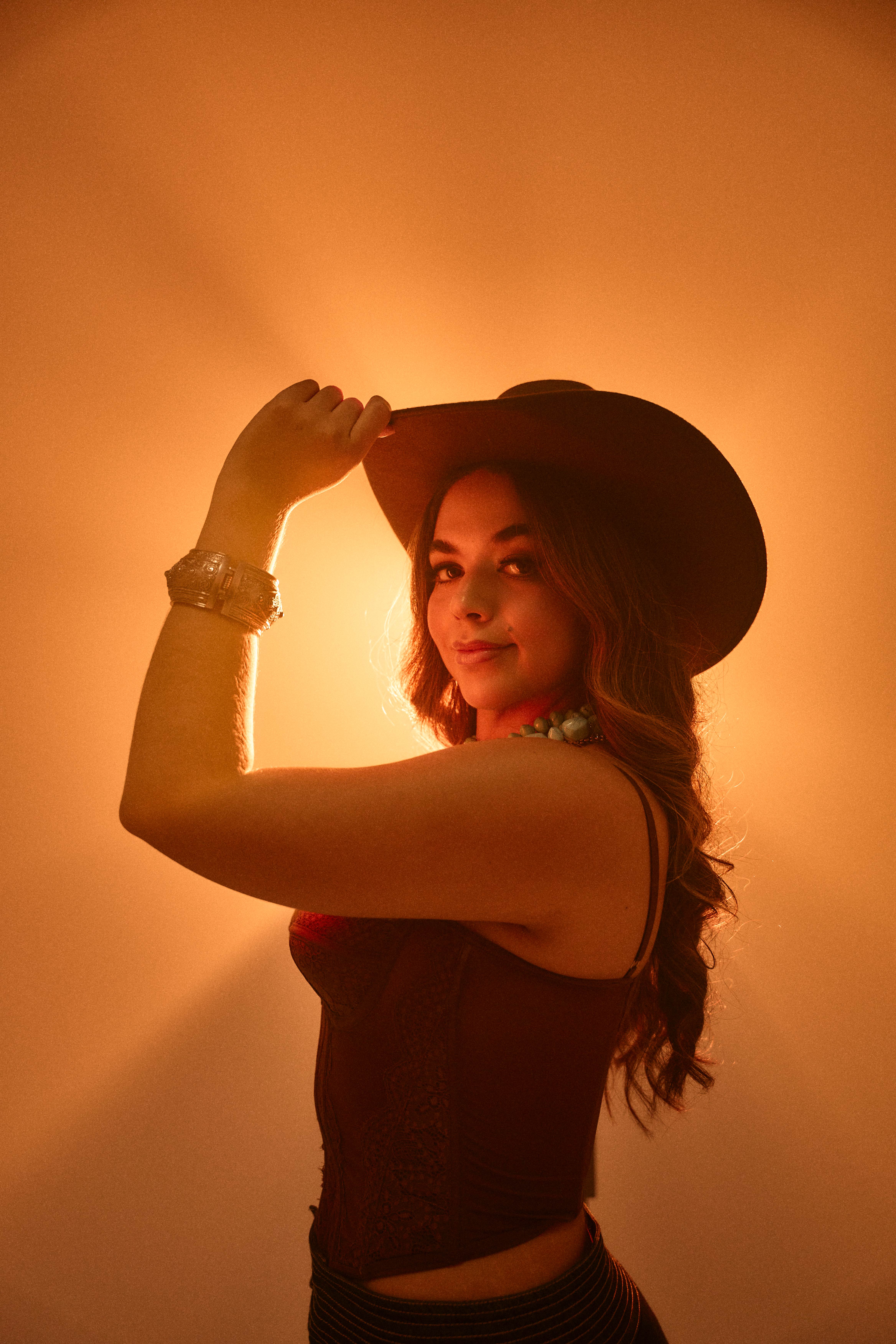 Mujer con sombrero vaquero a contraluz sobre fondo naranja cálido