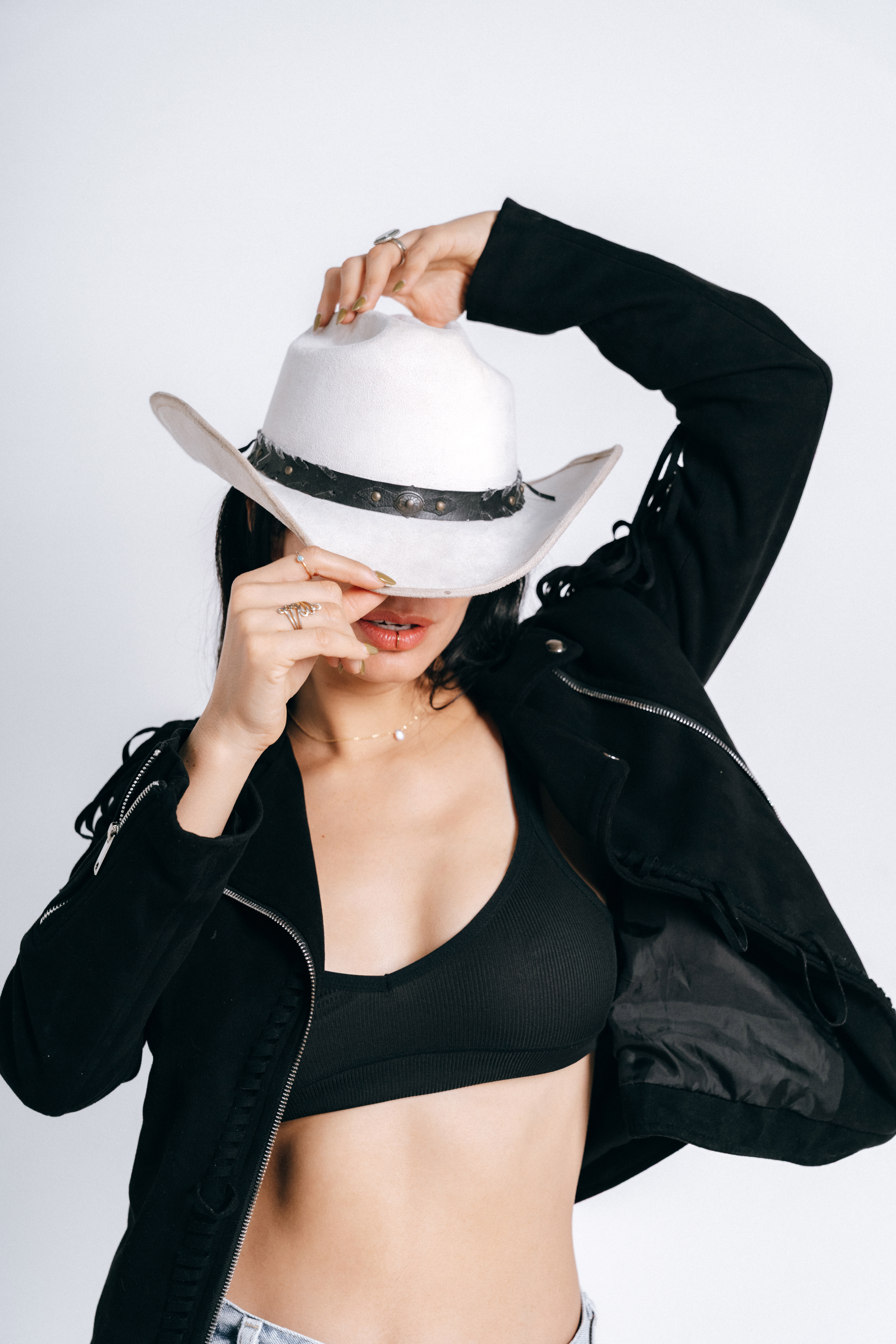 Mujer con sombrero vaquero blanco y chaqueta negra de flecos sobre fondo blanco