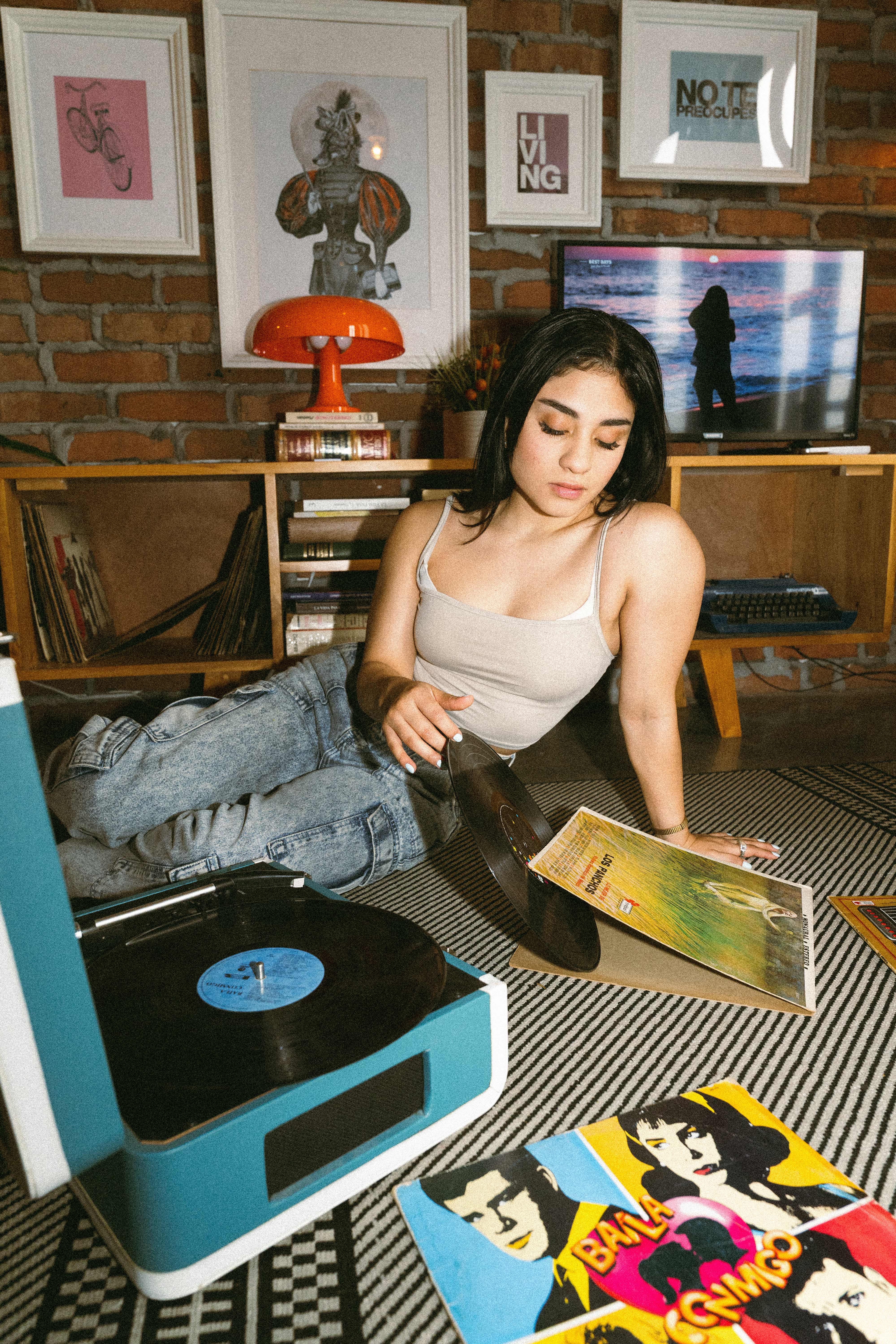 Mujer sentada en el piso junto a un tocadiscos turquesa y portadas de vinilos