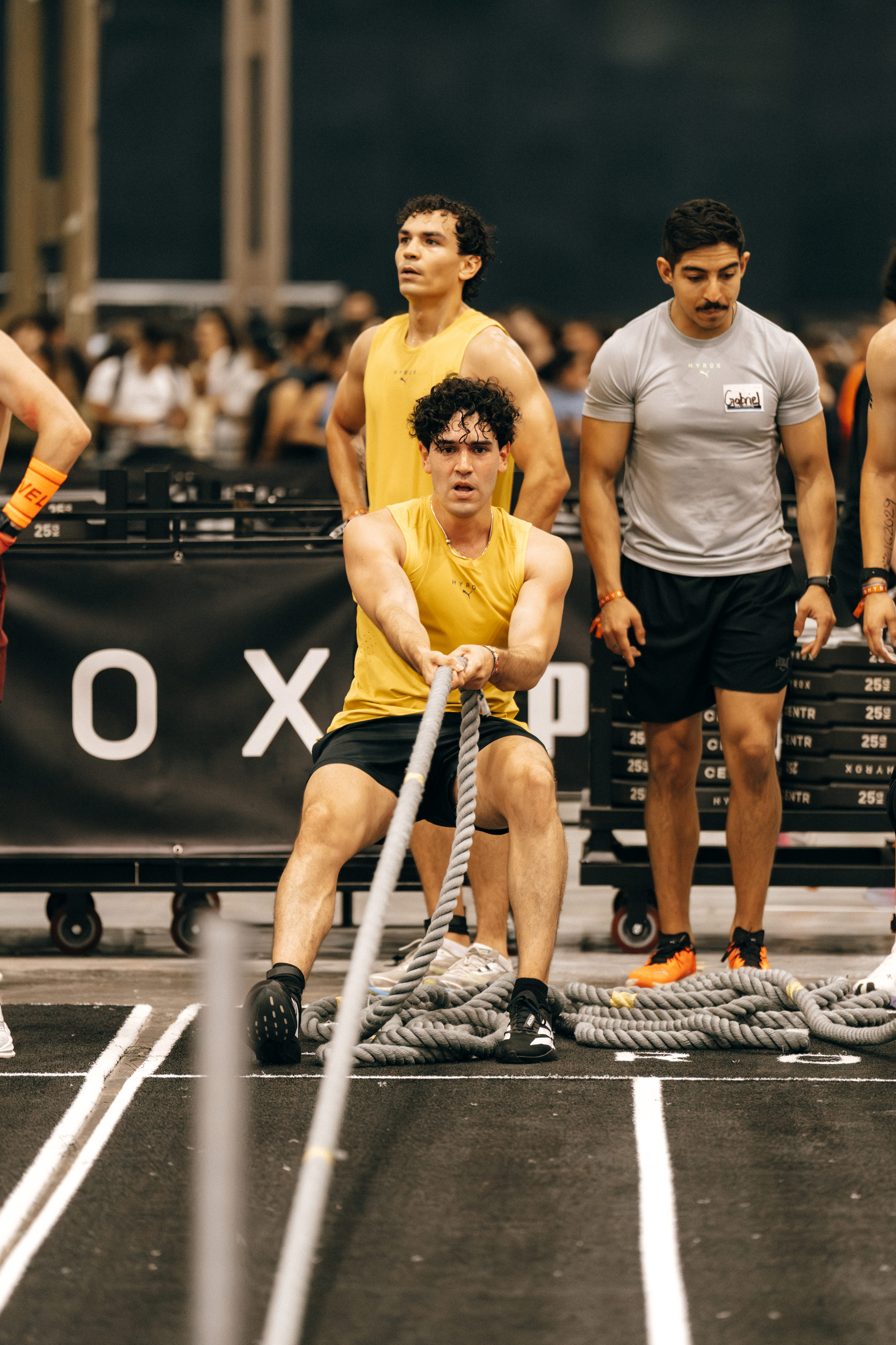 Competidor jalando una cuerda pesada mientras otros observan en una competencia de fitness