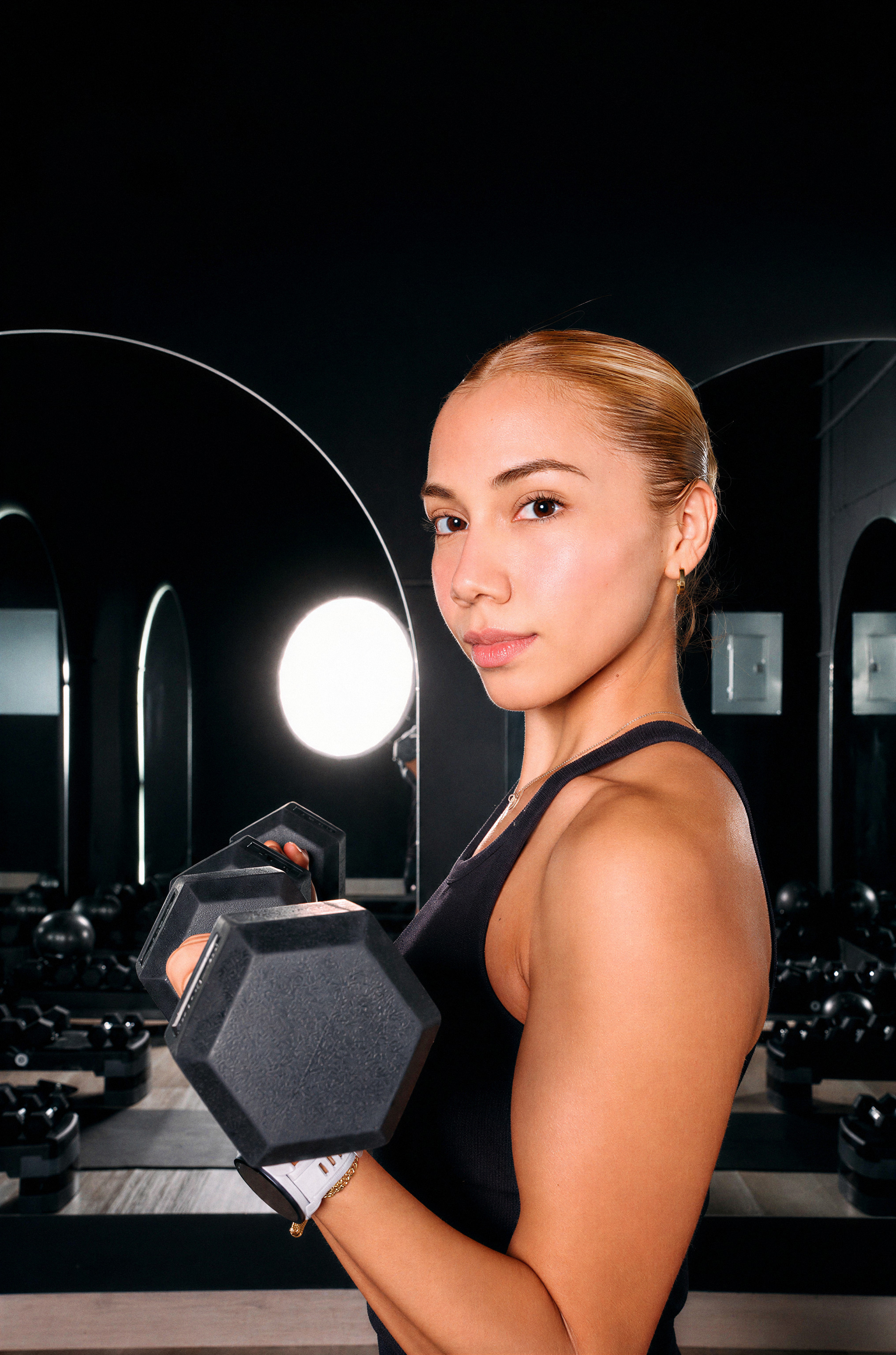 Mujer levantando una mancuerna hexagonal en un gimnasio oscuro