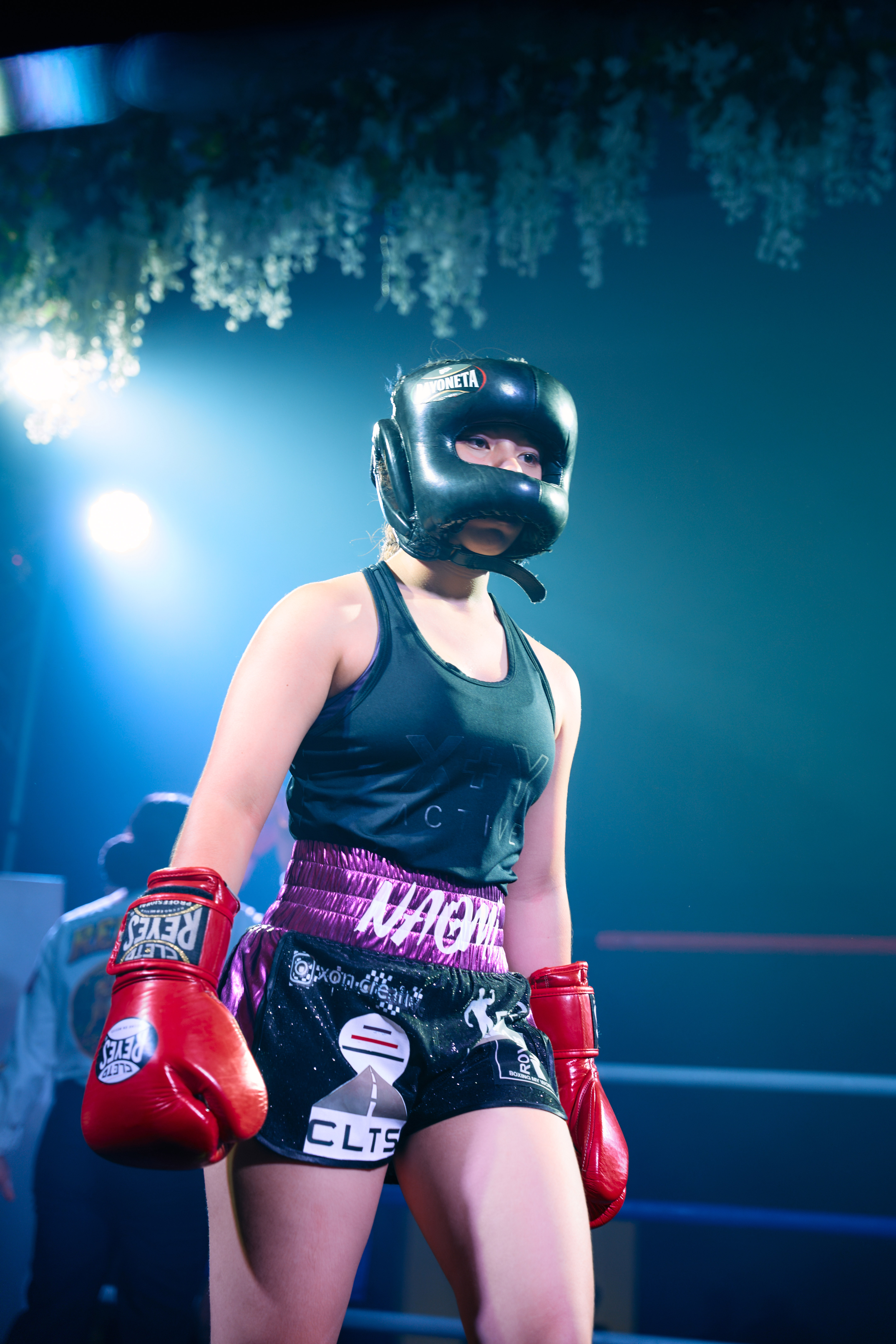 Boxeadora con careta y guantes rojos bajo las luces azules del ring