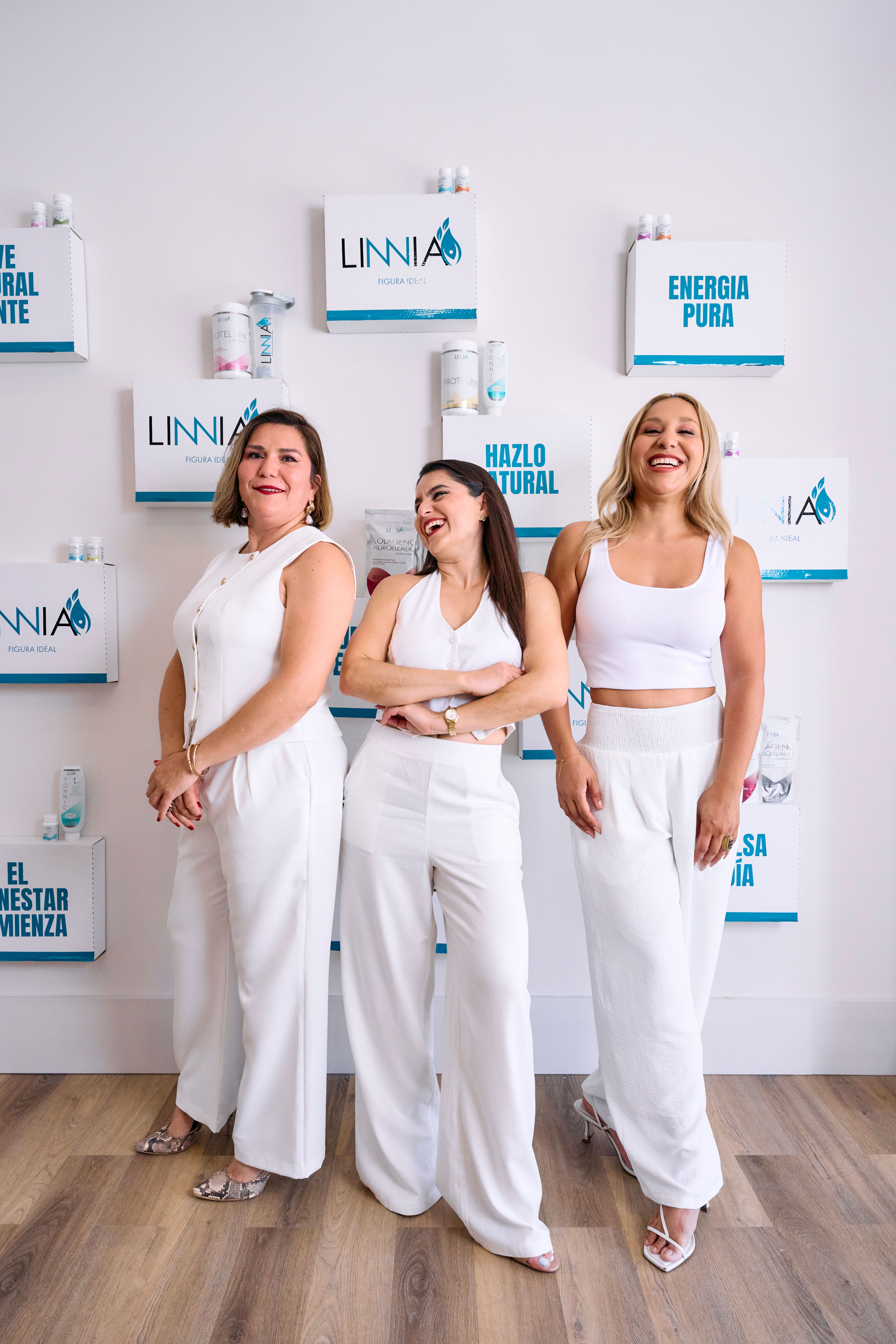 Tres mujeres vestidas de blanco frente a un muro de marca de LINNIA