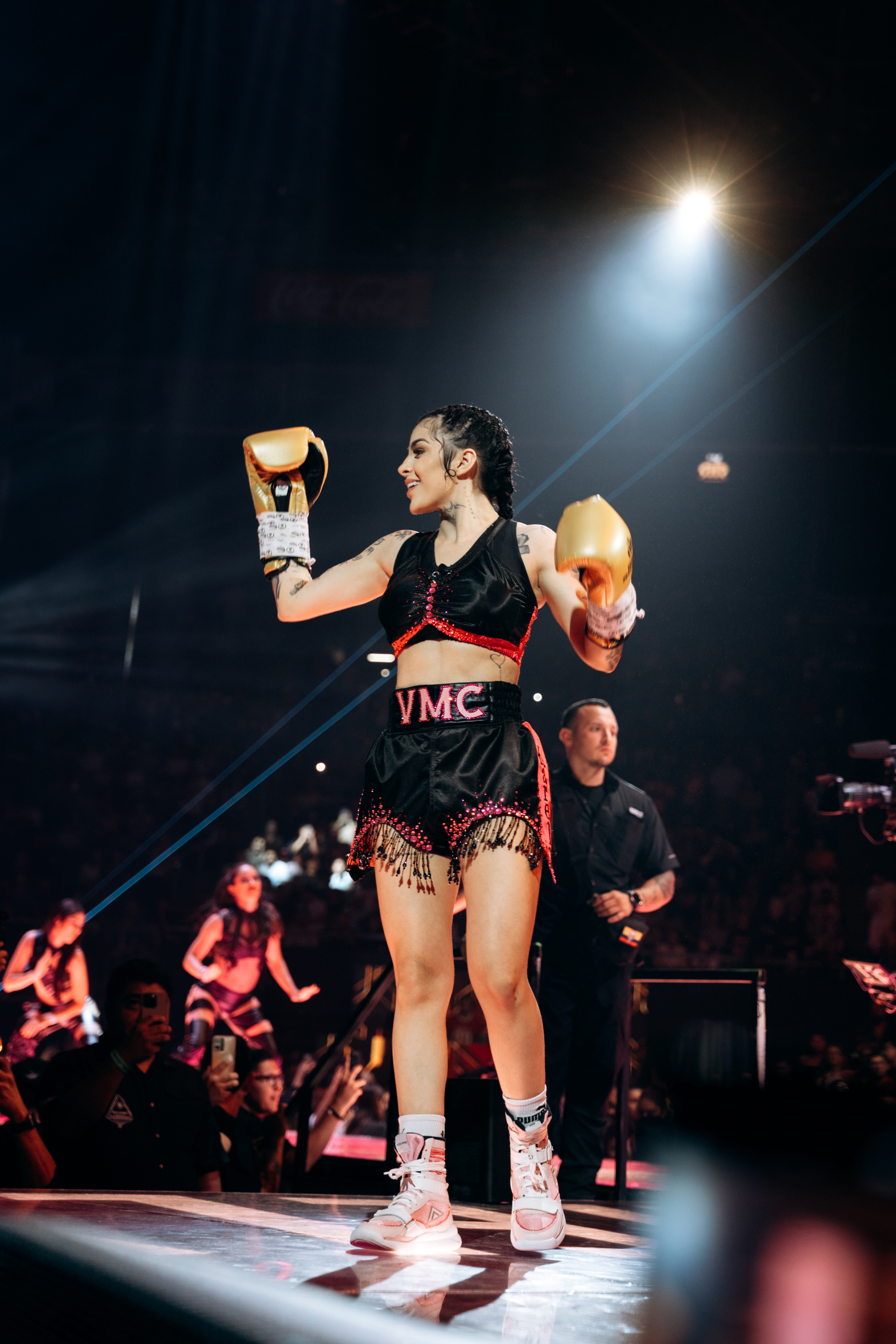 Boxeadora celebrando con guantes dorados en el ring frente al público