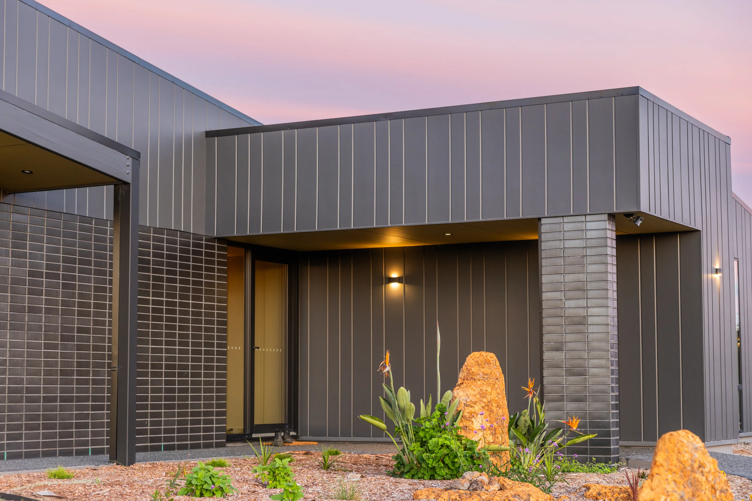 Entry porch with dark vertical cladding and glazed brick base at dusk