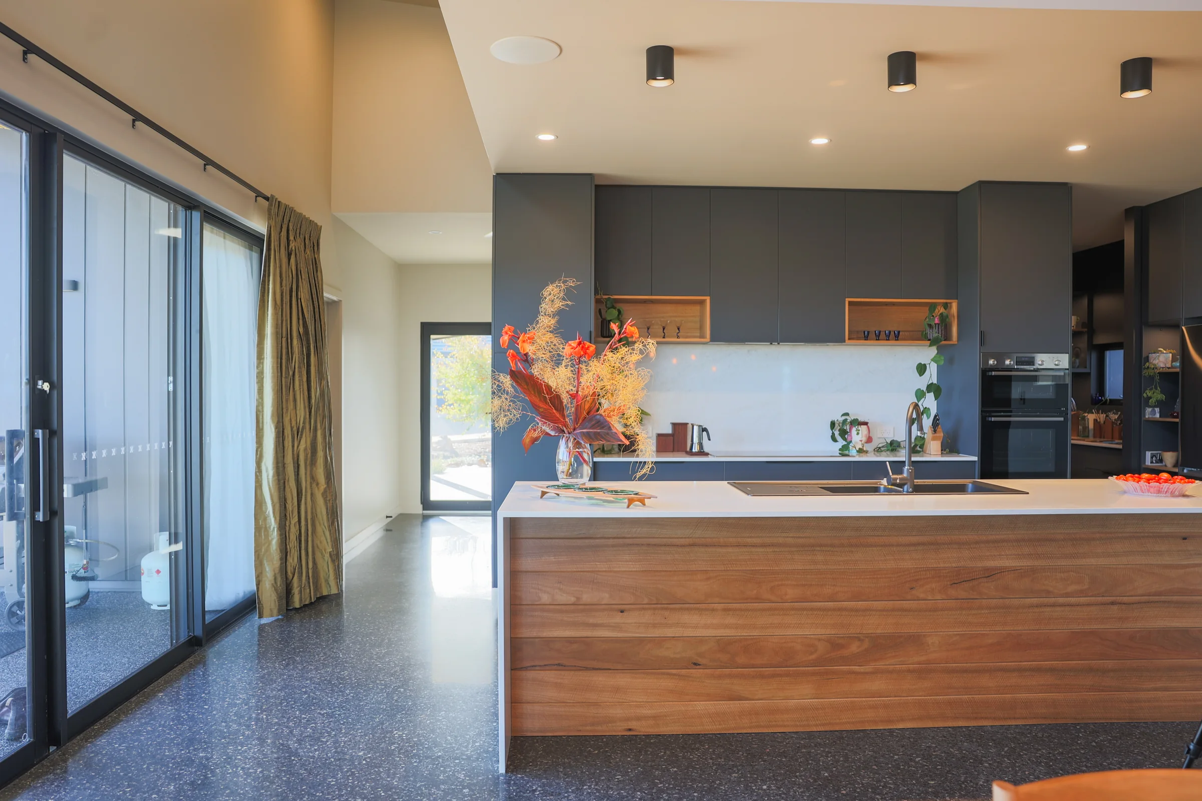 Kitchen island with timber panel front beside full-height glass doors