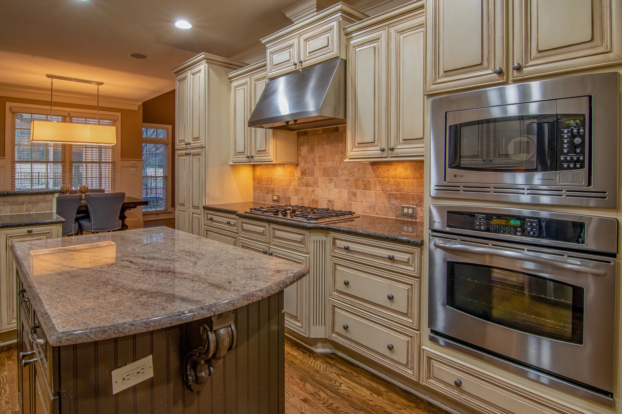 Kitchen with cream glazed cabinets, wall ovens, and a granite island