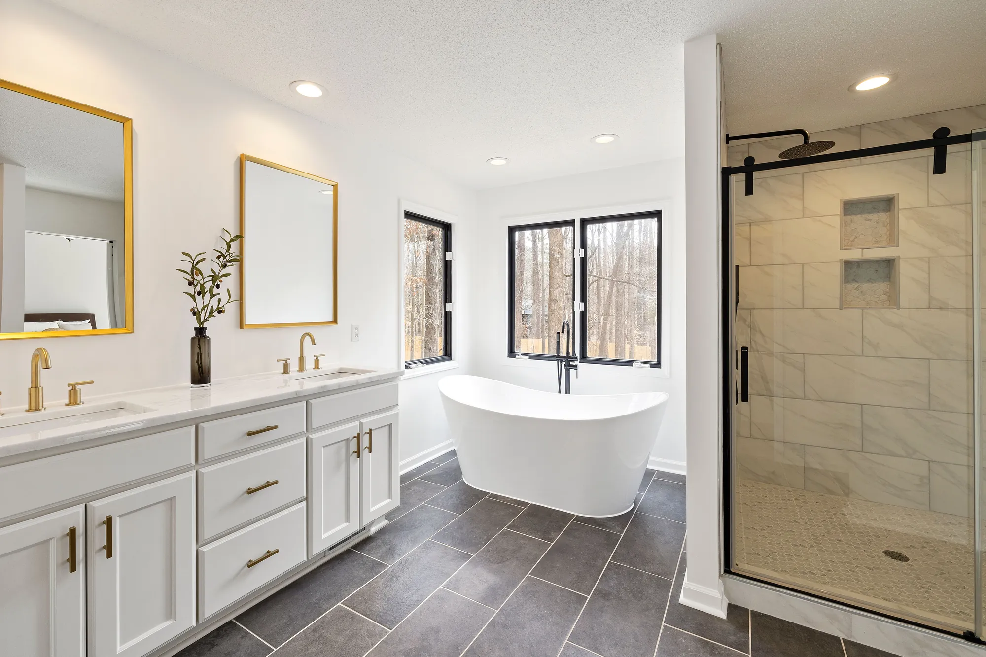 Bright bathroom with a freestanding white tub, a white double vanity with brass fixtures and a glass walk-in shower