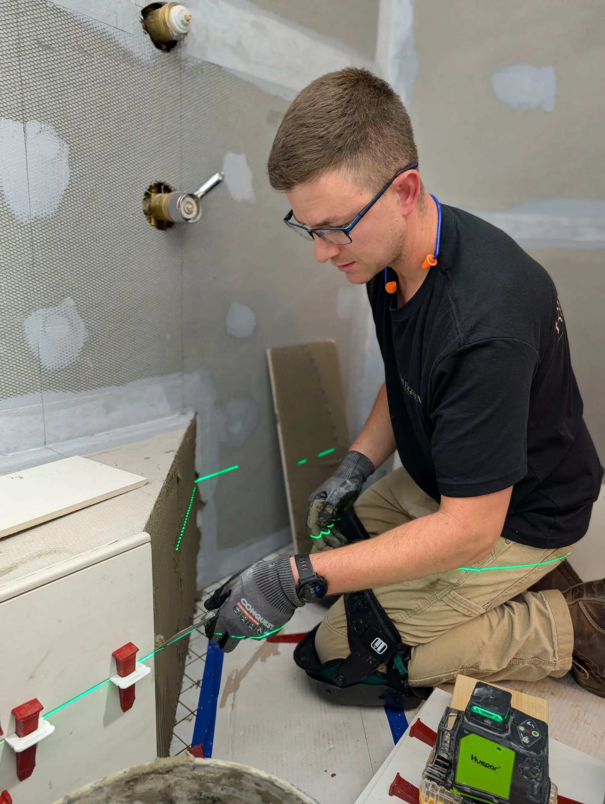 Austin Lapp of RiverGreen Remodeling setting shower wall tile with a green laser level marking the layout lines