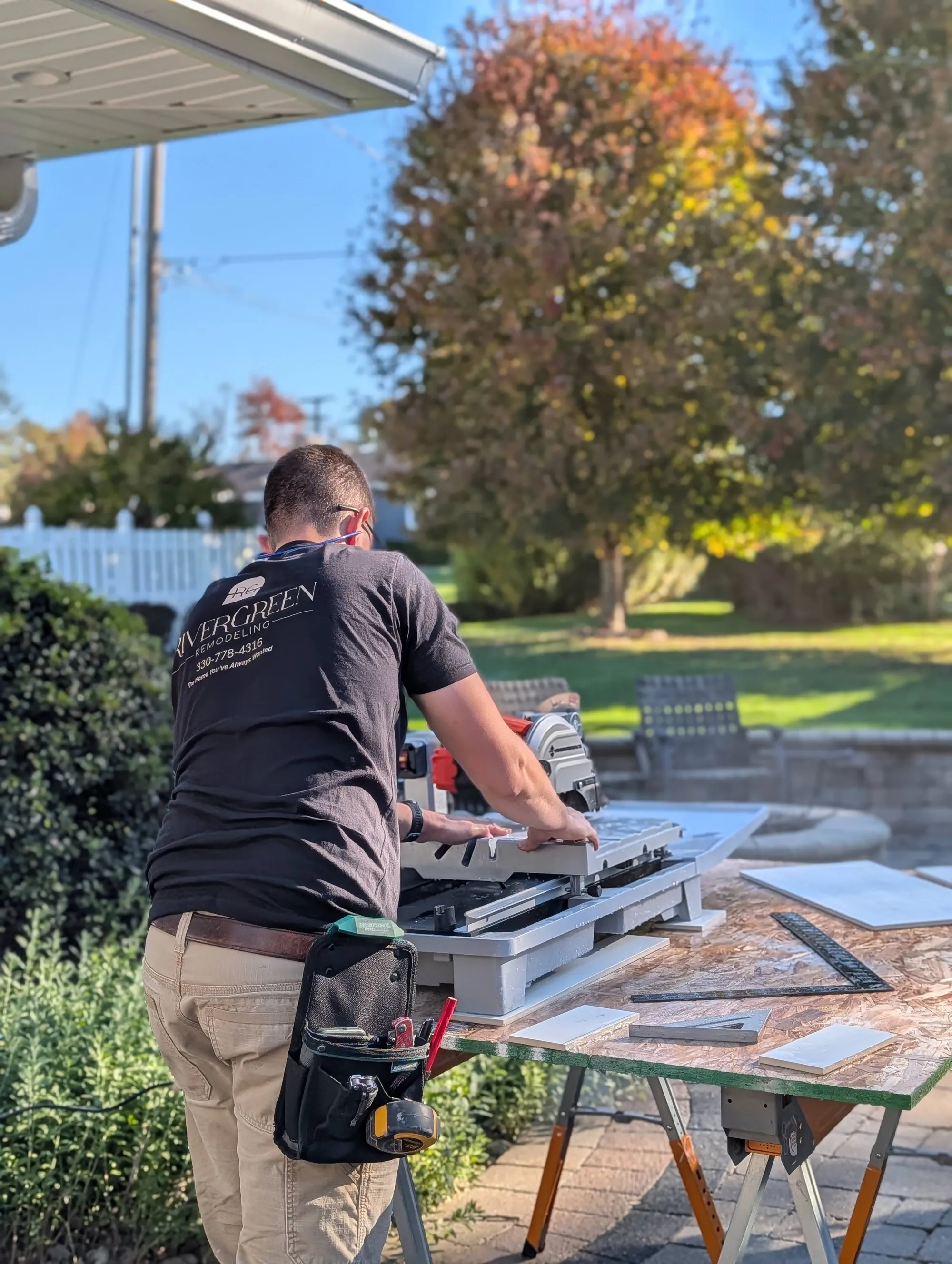 RiverGreen Remodeling crew member cutting tile on a wet saw set up on sawhorses at a job site