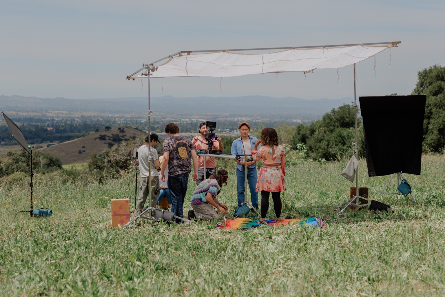 Outdoor film production with crew, camera and overhead diffusion.