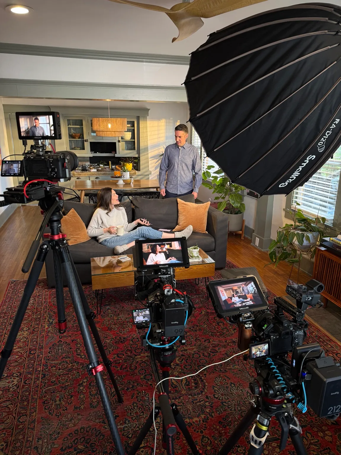 Behind the scenes of a living-room scene with three cameras, monitors and a large softbox.