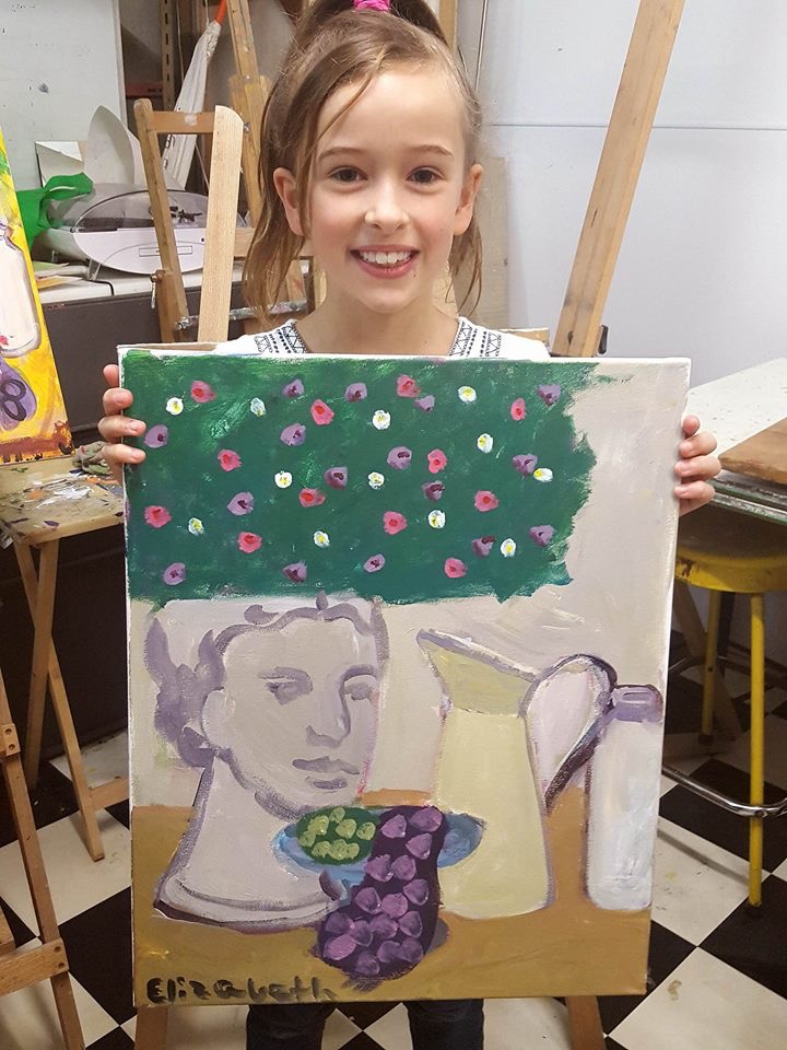 A student proudly holding up a finished painting at Art Studio 48