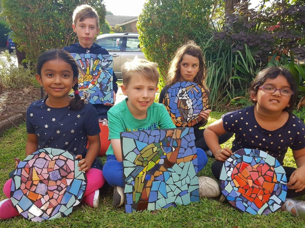 Students holding up their mosaic artwork with a dog