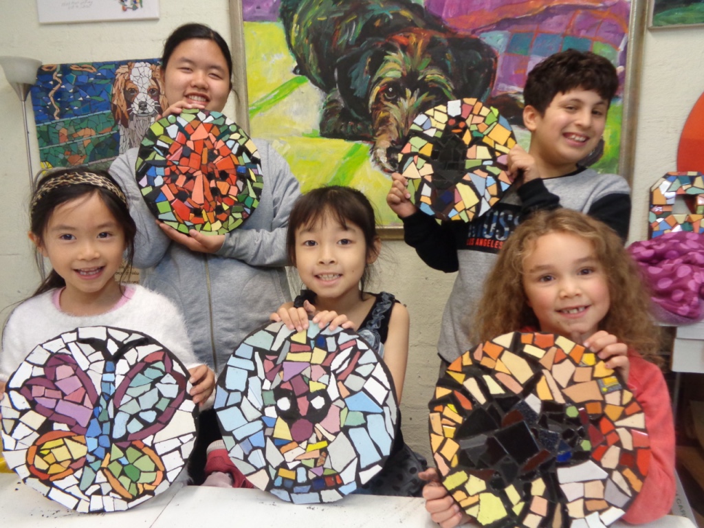 Students holding up their round mosaic artworks