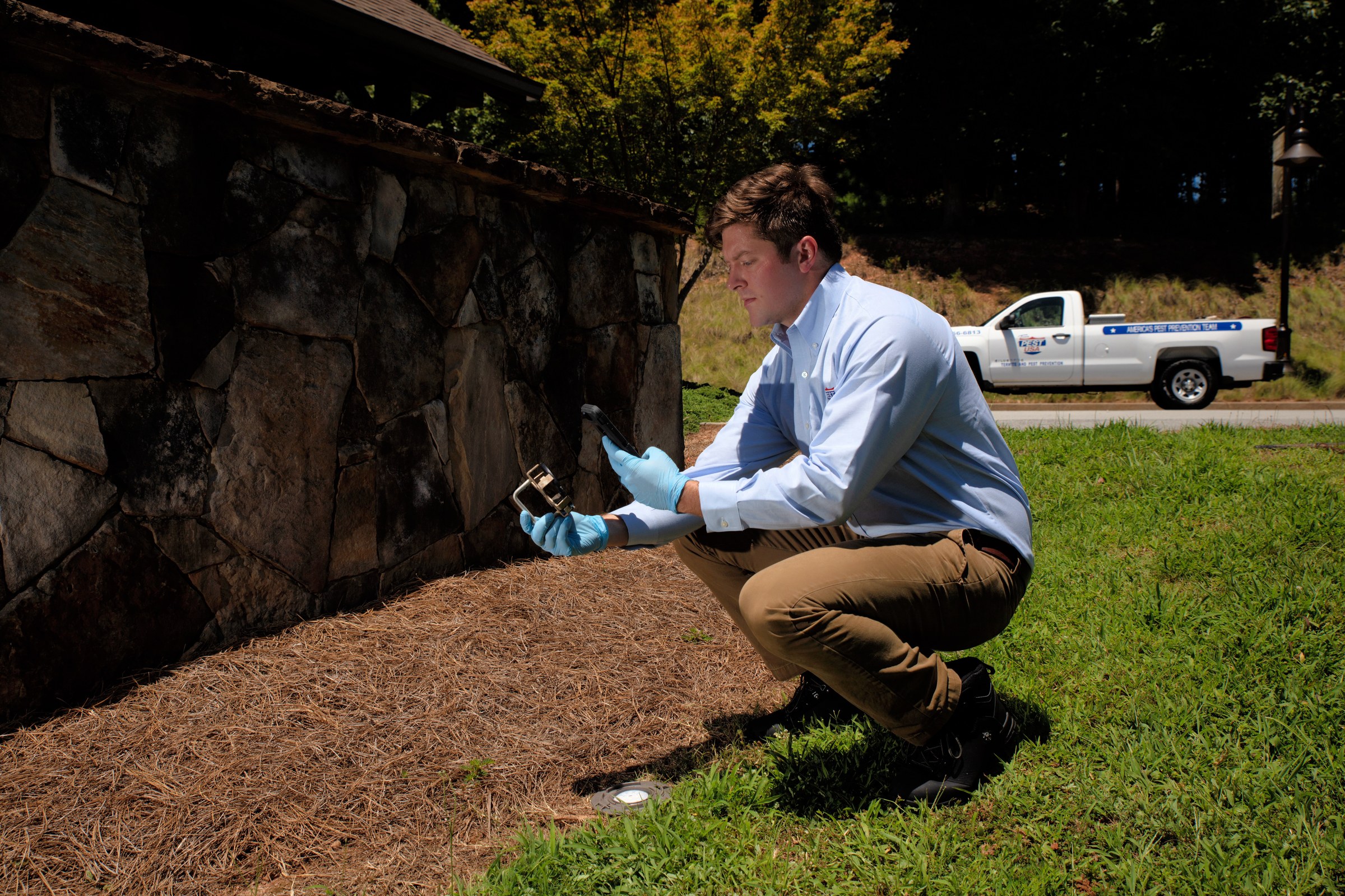Team Pest USA technician inspecting an exterior wall with handheld equipment.