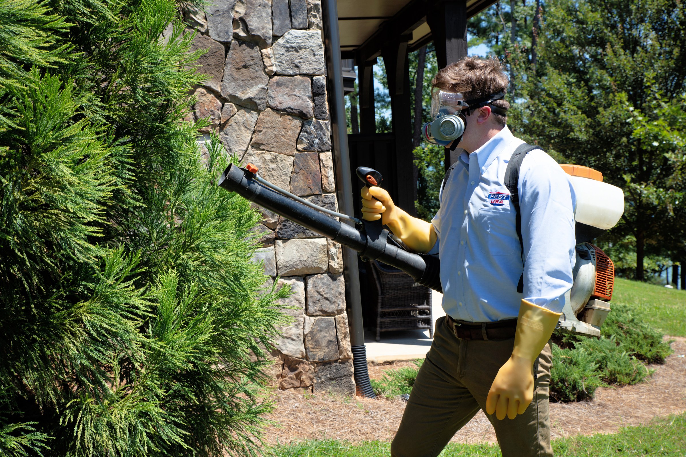 Team Pest USA technician applying an exterior pest treatment with backpack equipment.
