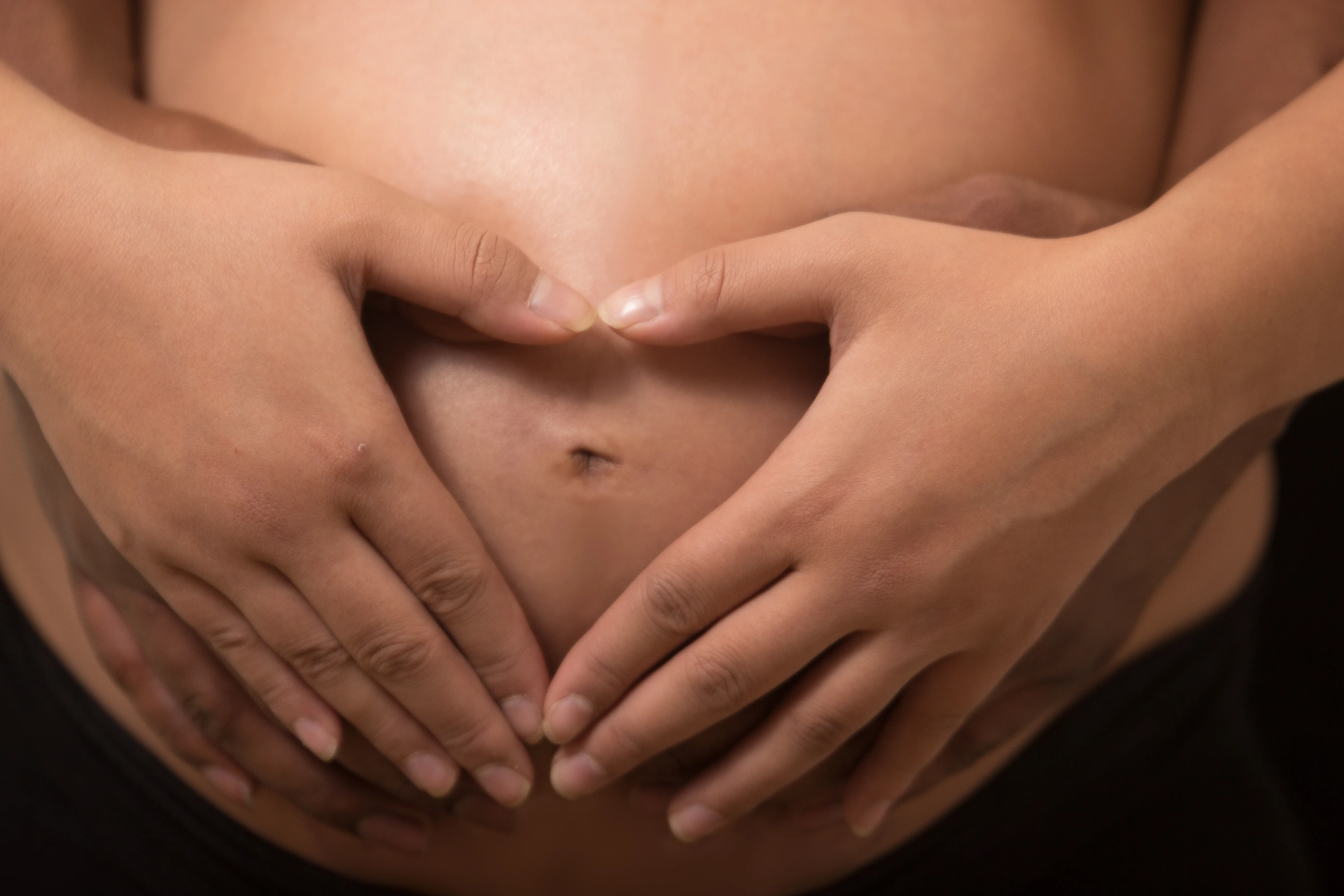 Hands forming a heart around Kristen's belly during an at-home maternity session