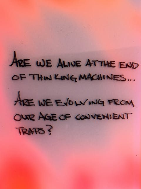 handwriting on a pink and red glow: are we alive at the end of thinking machines... are we evolving from our age of convenient traps?