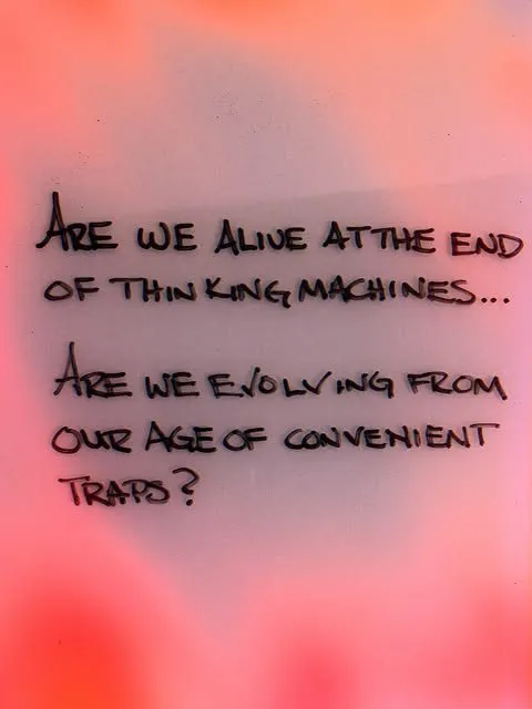 handwriting on a pink and red glow: are we alive at the end of thinking machines... are we evolving from our age of convenient traps?